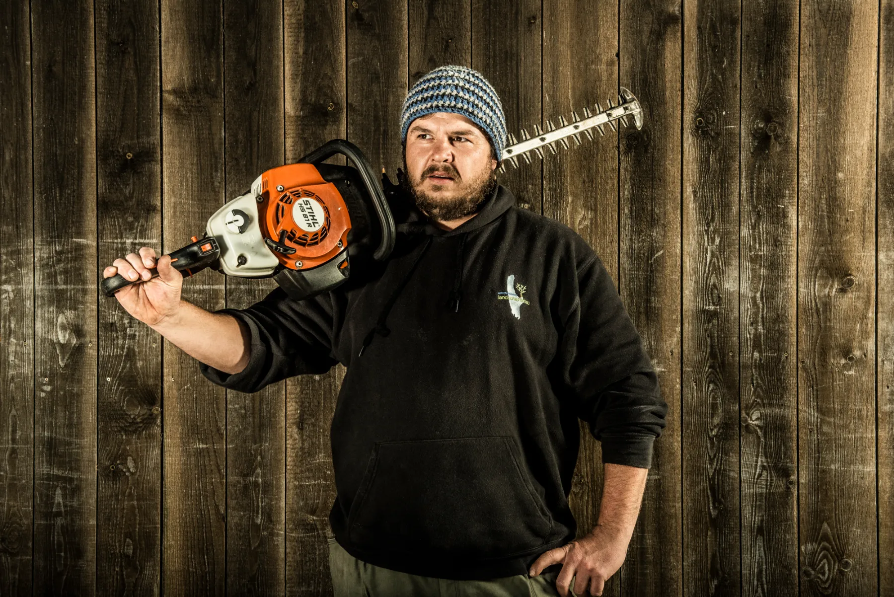 Bearded team member in a beanie carrying a hedge trimmer on his shoulder — brand photography by Janina Laszlo for Ammerseer Landschaftsbau, landscaping company in Bavaria