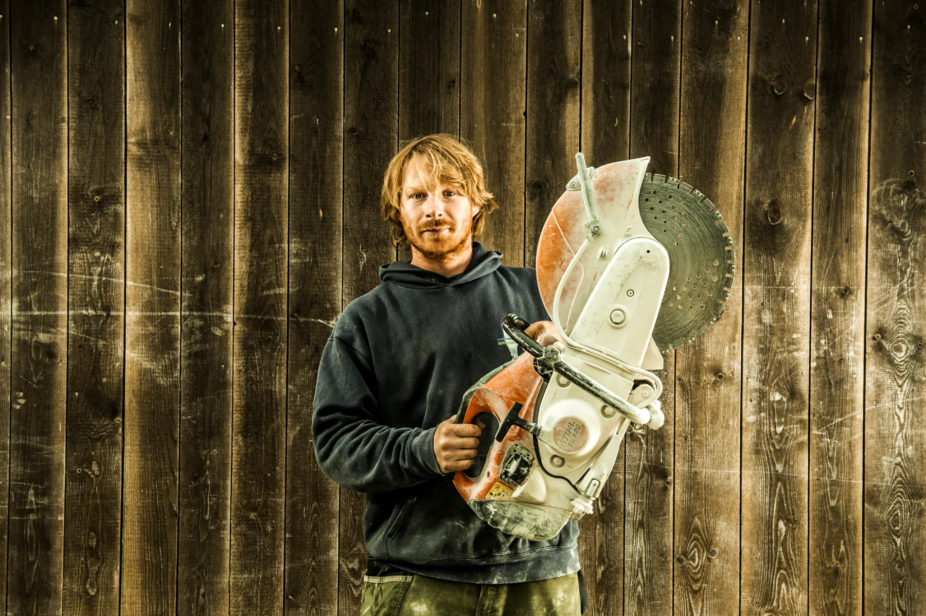 Red-bearded team member holding a cut-off saw — brand photography highlighting craftsmanship, by Janina Laszlo for Ammerseer Landschaftsbau in Bavaria, Germany