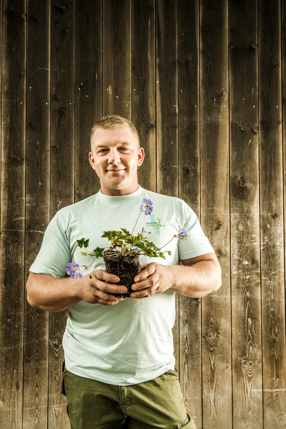 Team member in a white T-shirt holding a potted plant — brand photography by Janina Laszlo for Ammerseer Landschaftsbau, garden design and landscaping in Bavaria