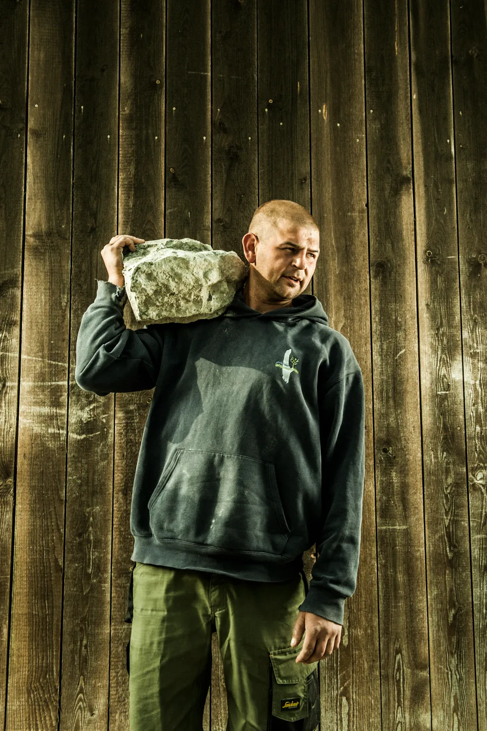 Team member carrying a natural stone on his shoulder — craftsmanship portrait by Janina Laszlo for Ammerseer Landschaftsbau, professional landscaping company in Bavaria