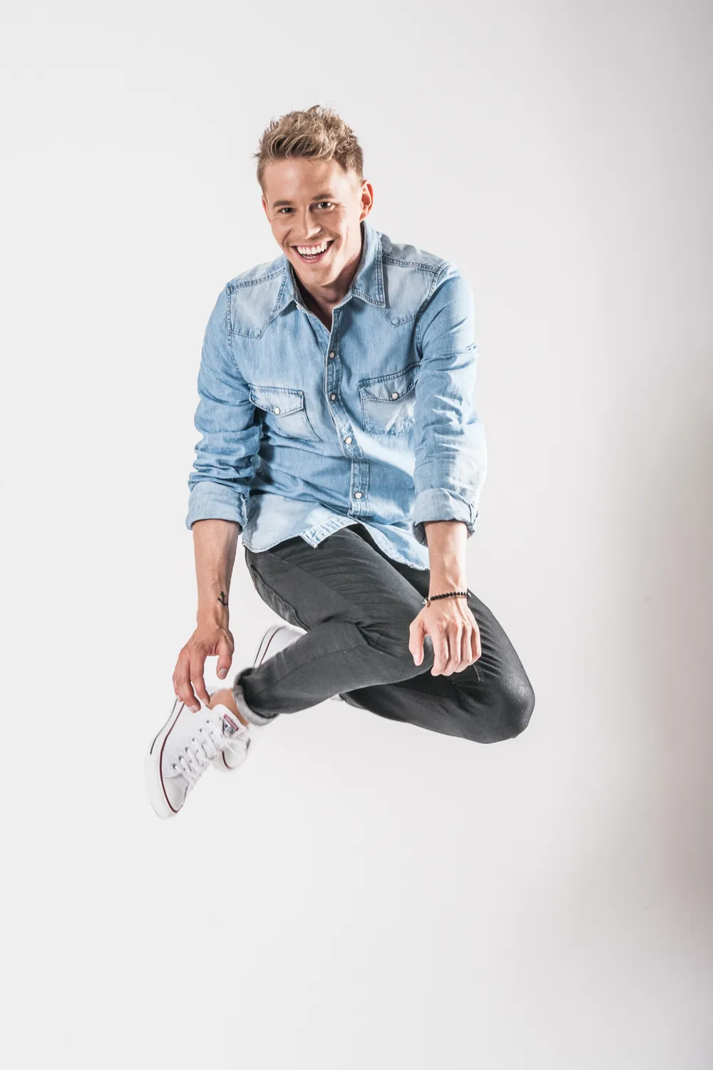 TV presenter Timo Killer jumping and laughing in a denim shirt against a white background — commercial advertising photography by Janina Laszlo for AOK