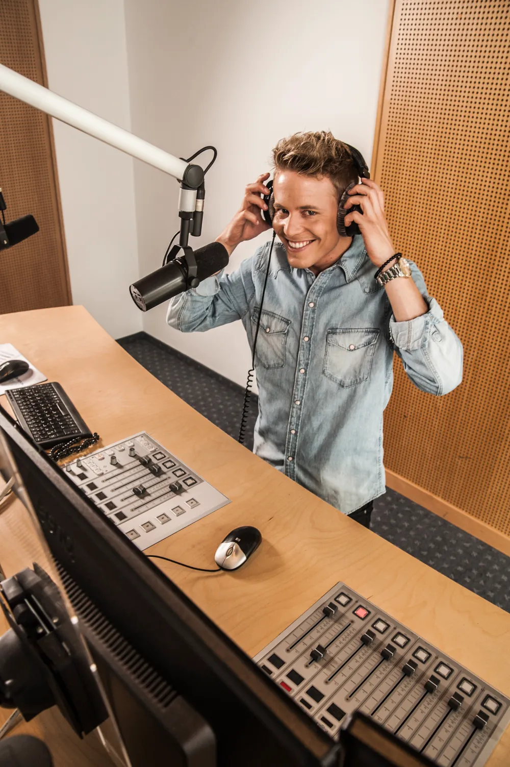 Timo Killer putting on headphones at a studio microphone, smiling up at the camera — commercial portrait photography by Janina Laszlo for AOK