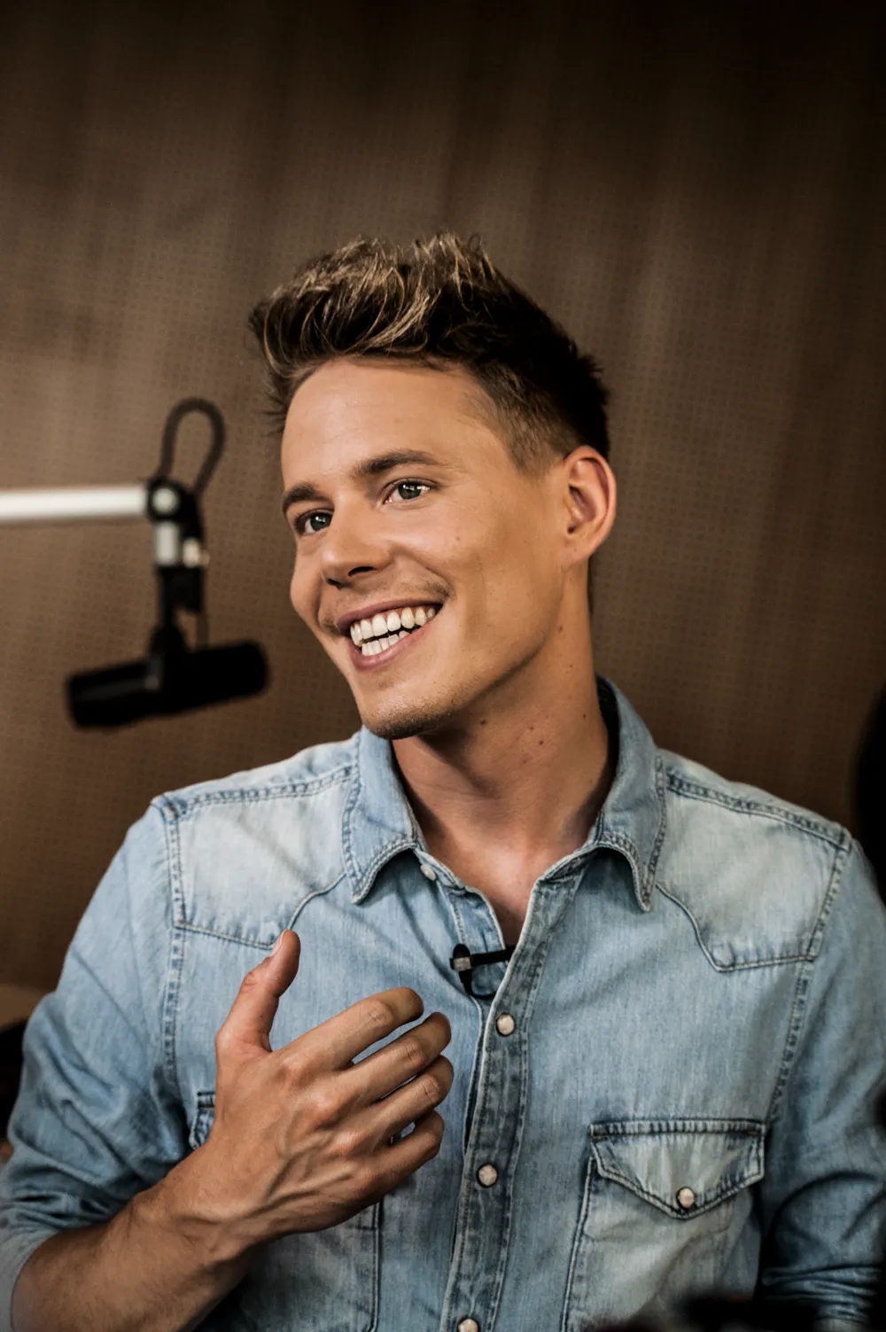 Close-up of TV presenter Timo Killer laughing in a denim shirt in front of a studio microphone — authentic visual storytelling for the AOK campaign by Janina Laszlo