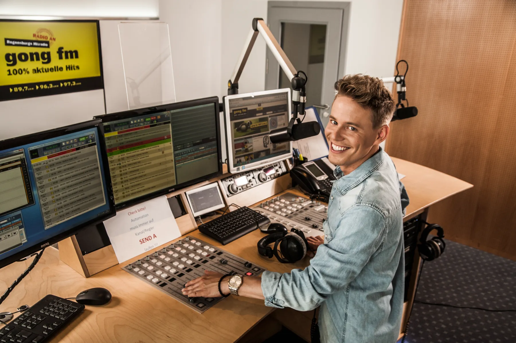 Timo Killer at a radio mixing desk, turning to smile at the camera — healthcare brand campaign photography by German photographer Janina Laszlo for AOK