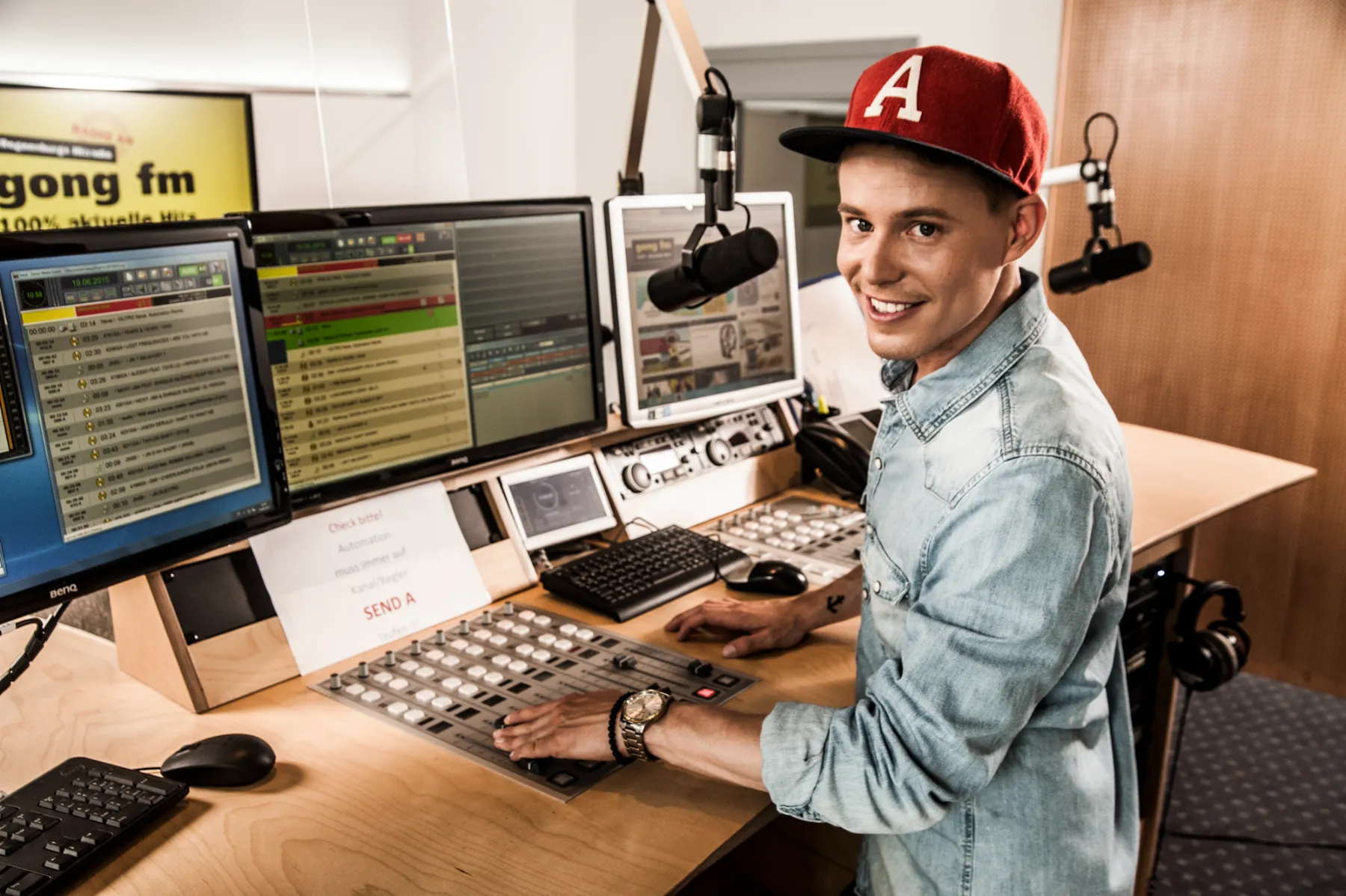 Timo Killer in a red baseball cap at the studio mixing desk — contemporary portrait for the AOK campaign by German photographer Janina Laszlo