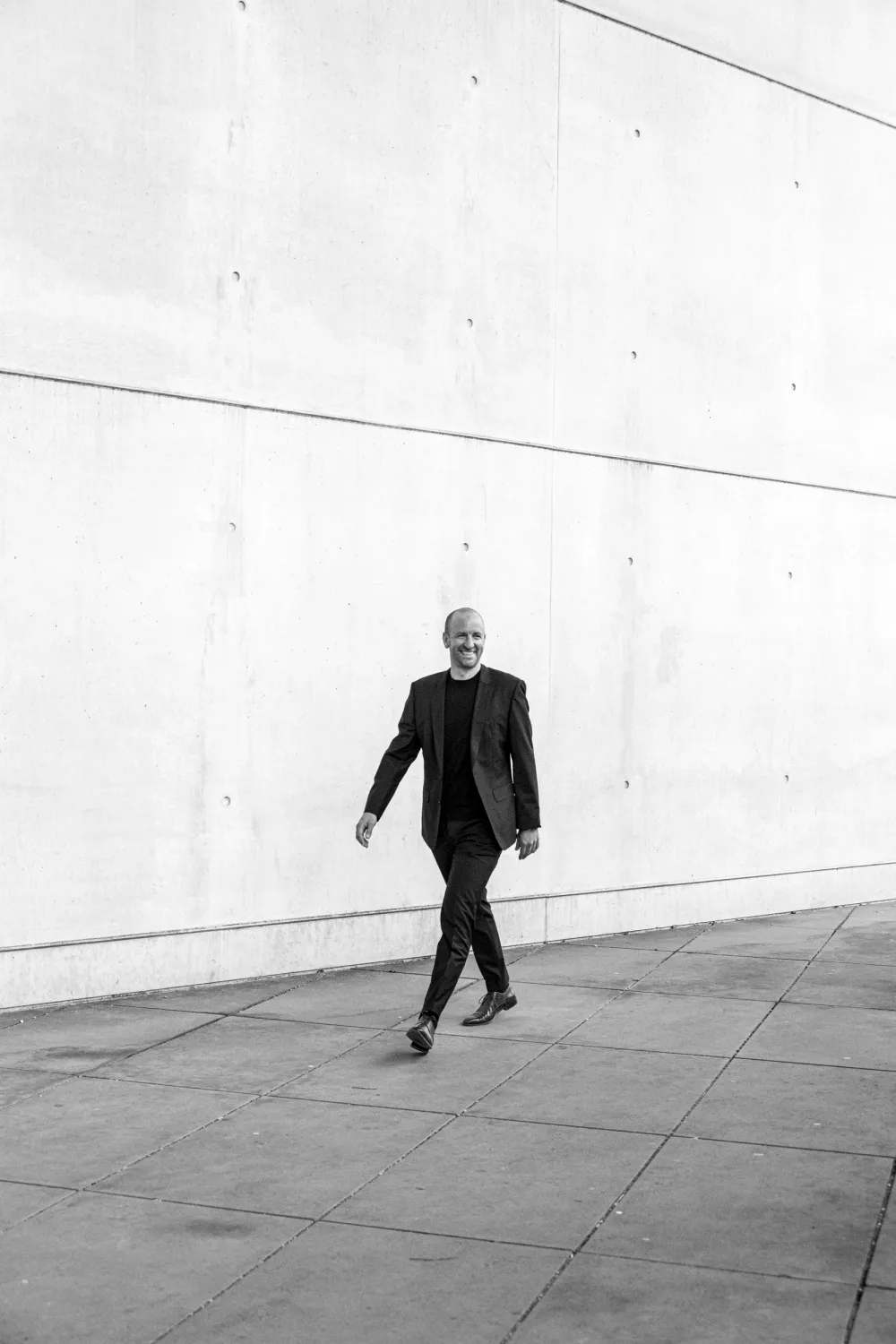 Architect walking past a long white concrete wall, black-and-white — architectural office Helmling — portrait by Janina Laszlo, portrait photographer in Munich