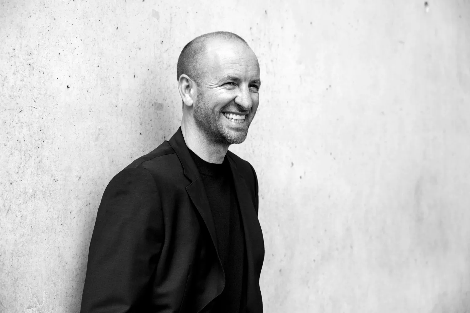 Smiling architect leaning against a concrete wall, black-and-white portrait — architectural office Helmling — portrait by Janina Laszlo, portrait photographer in Munich
