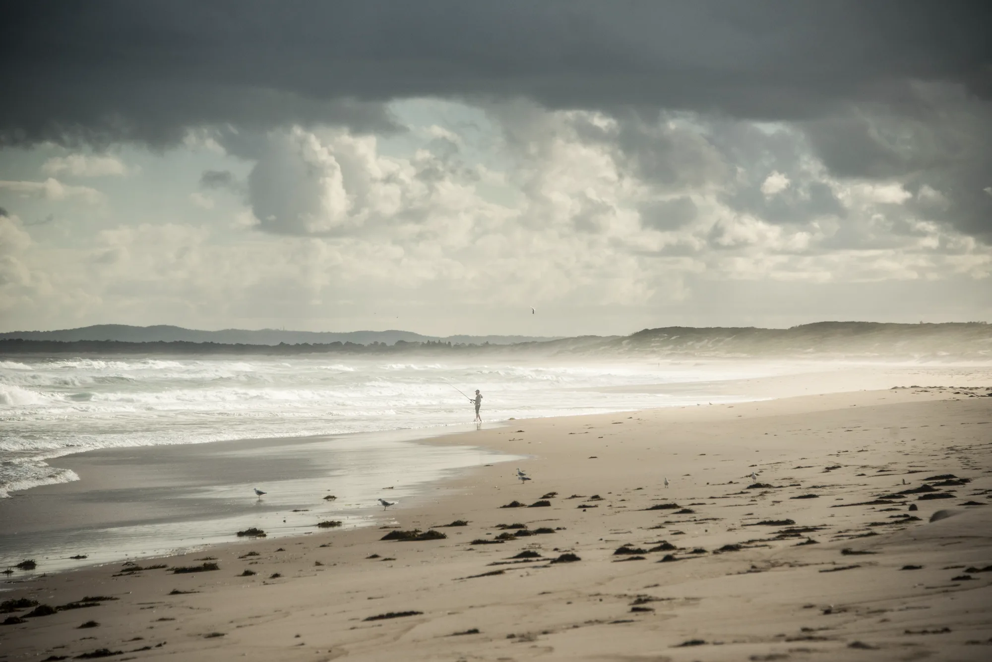 Fisherman casting into the surf on a wide beach under storm clouds — Australia, travel and fine art photography by Janina Laszlo