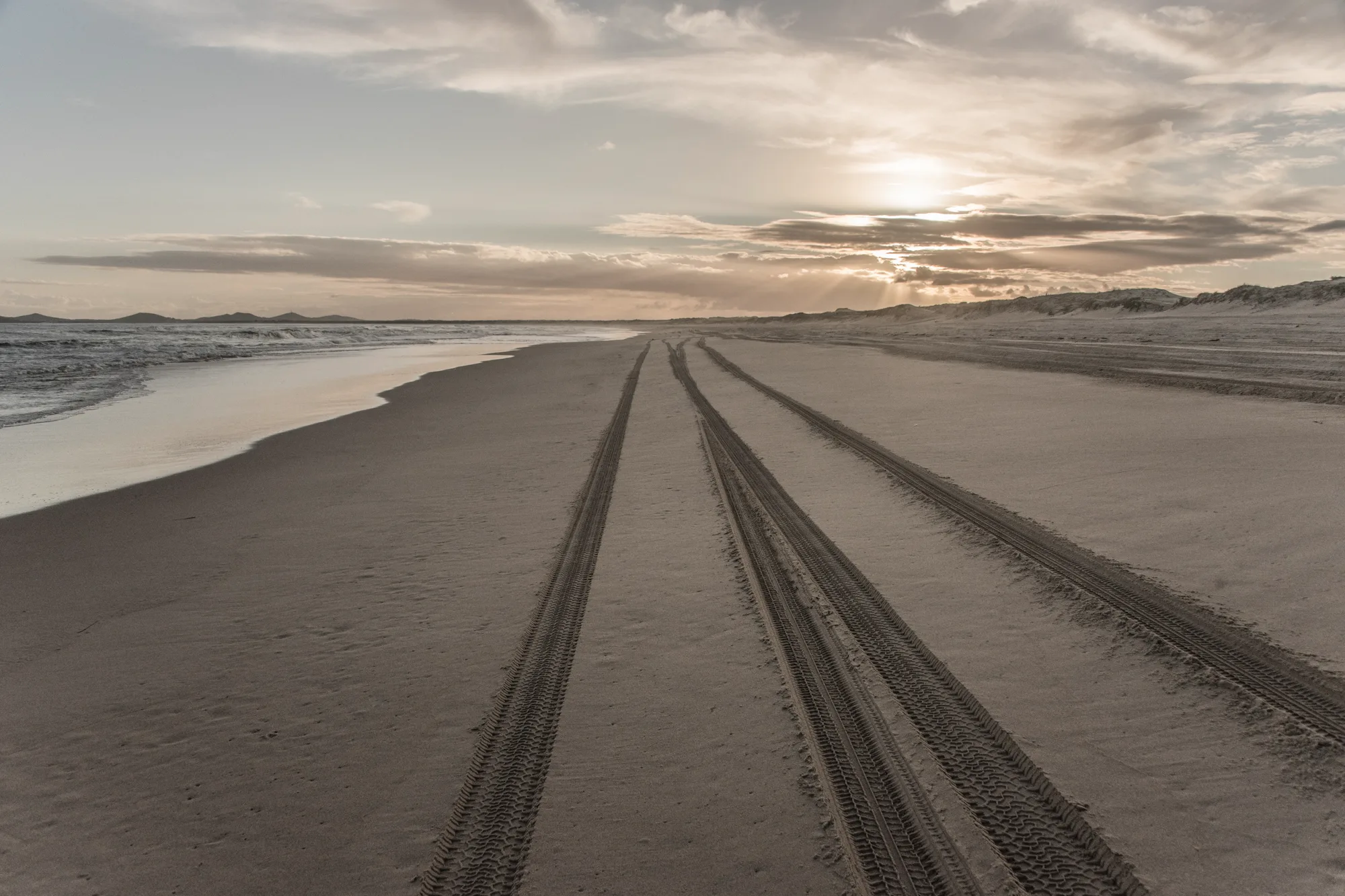 Tyre tracks running along a long beach towards the setting sun — Australia, travel and fine art photography by Janina Laszlo
