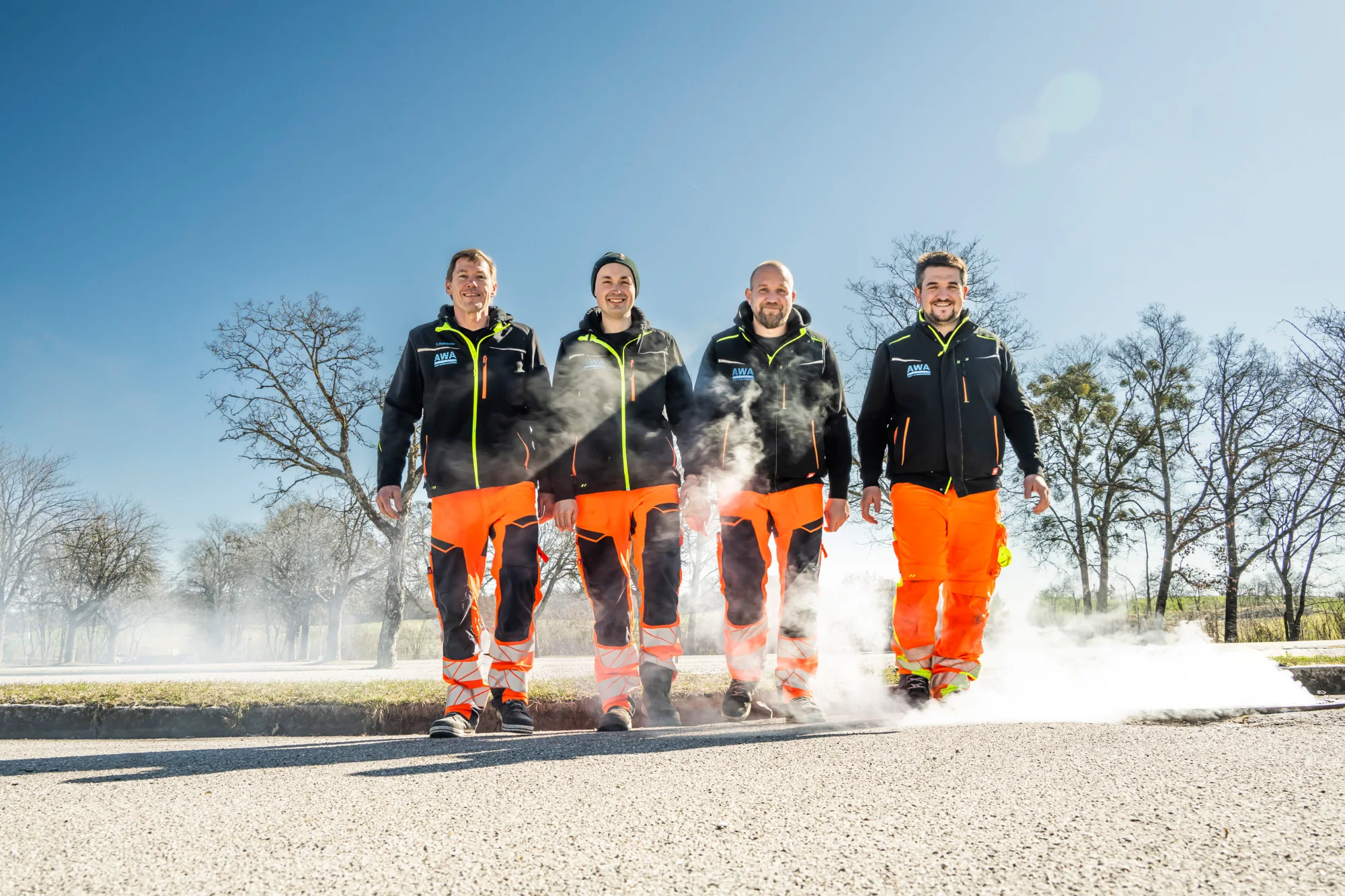 Wastewater team in orange and black workwear walking through steam on a sunny winter road — AWA Ammersee, industrial, corporate and portrait photography by Janina Laszlo