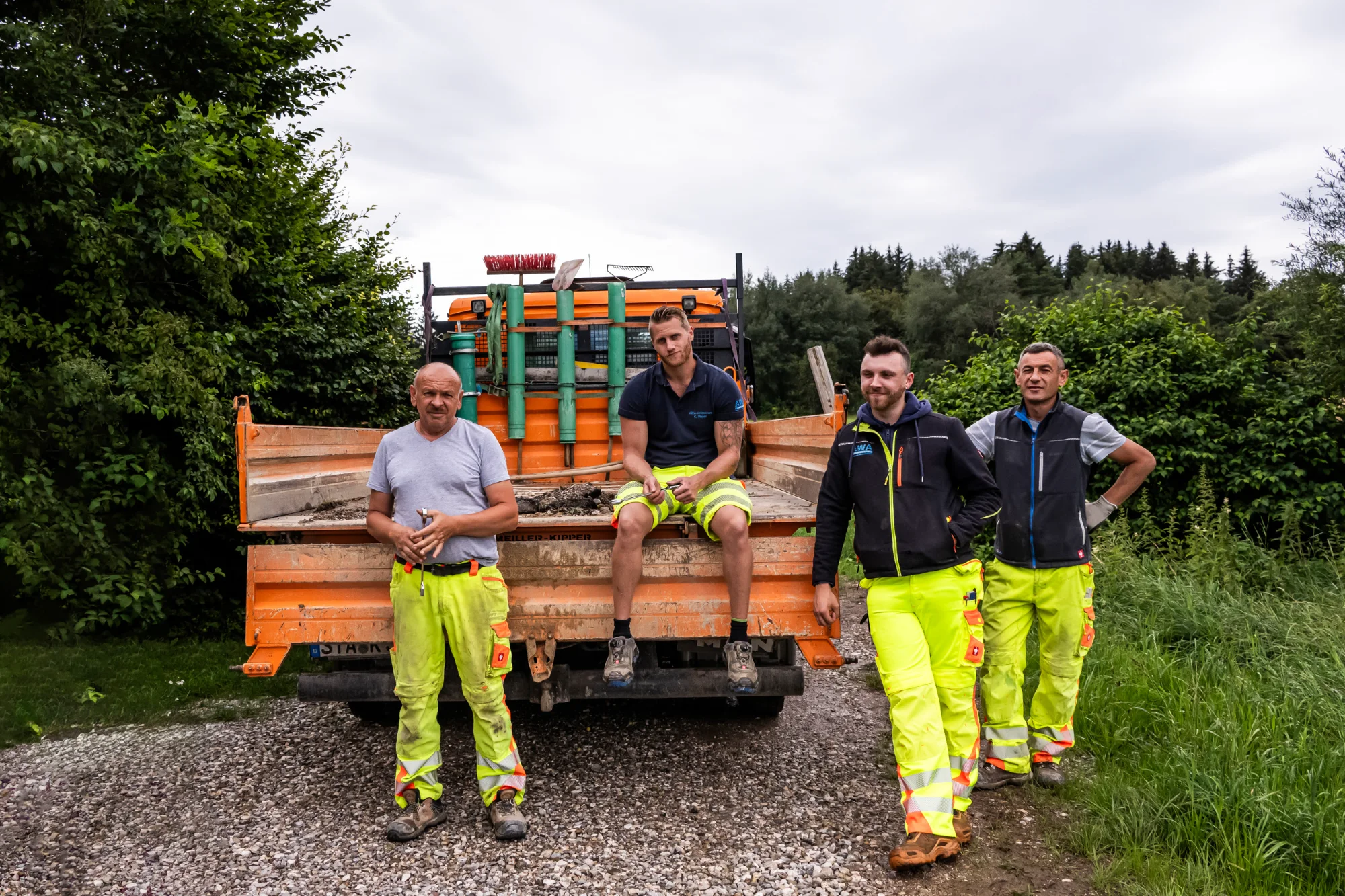 Pipe-laying crew in hi-vis workwear posing in front of a loaded orange tipper truck — AWA Ammersee, industrial, corporate and portrait photography by Janina Laszlo