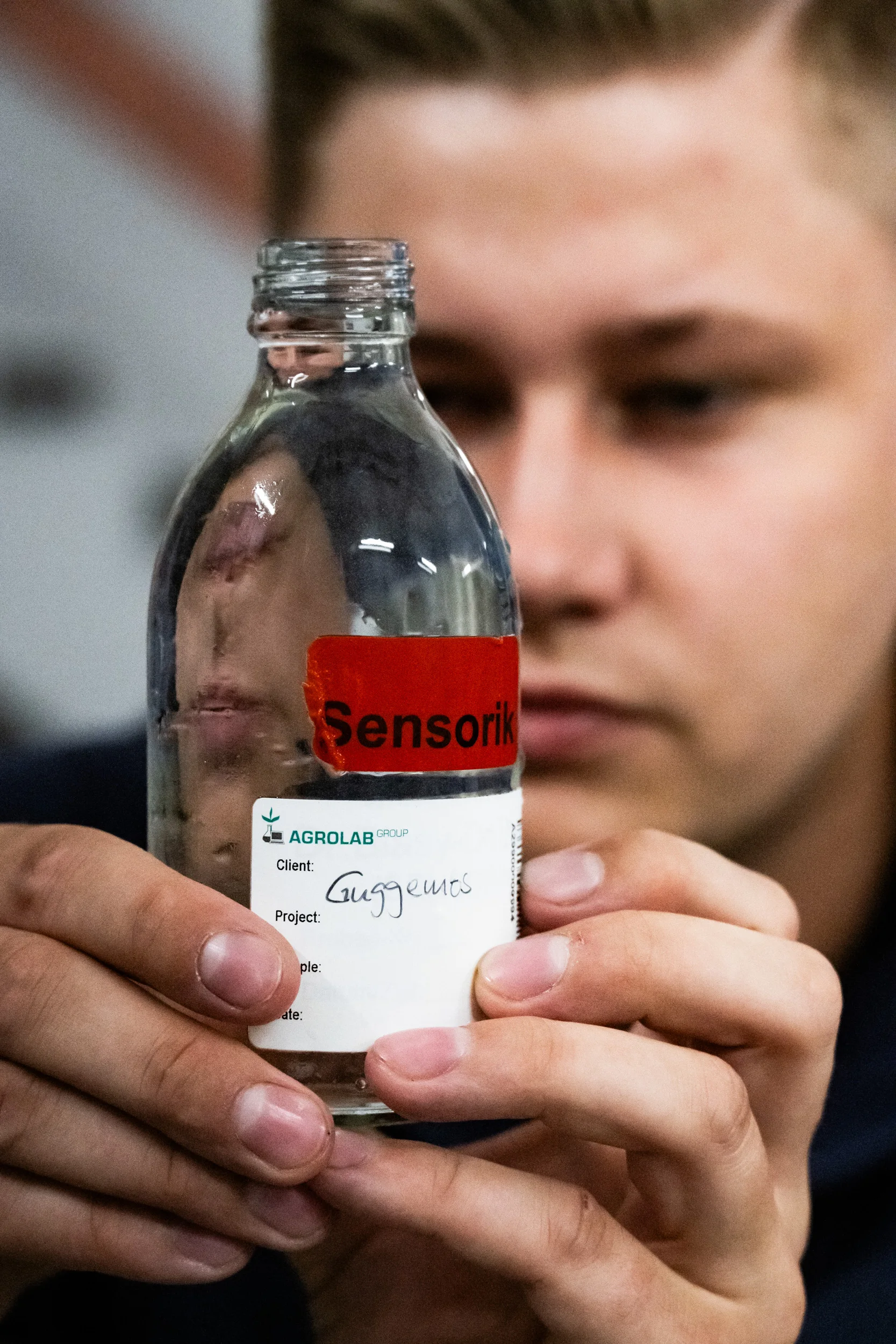 Young technician holding up a labelled glass bottle of drinking water sample — AWA Ammersee, industrial, corporate and portrait photography by Janina Laszlo