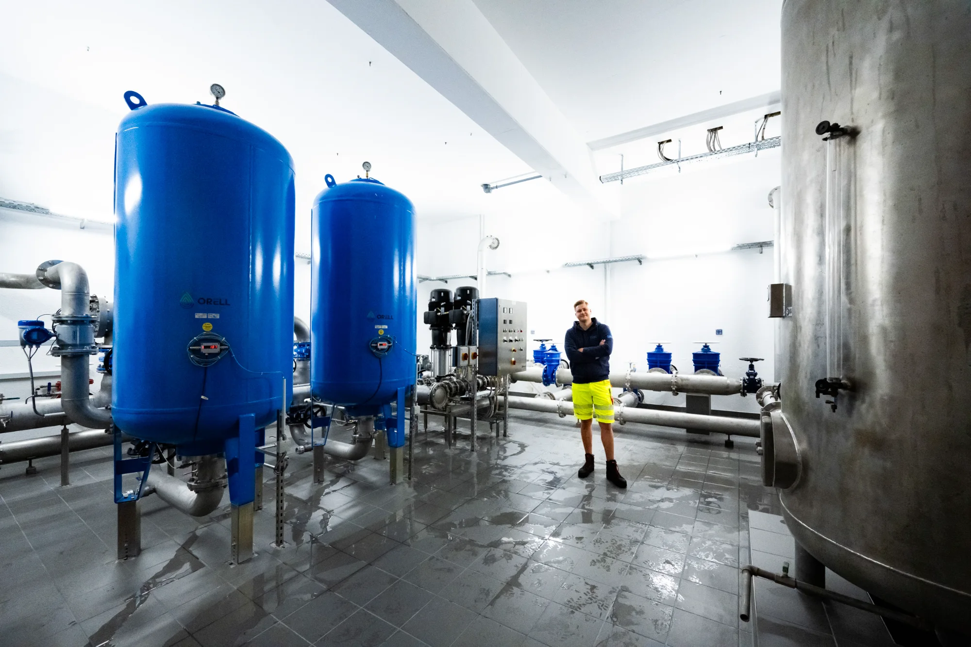 Employee standing among blue pressure tanks in a bright waterworks hall — AWA Ammersee, industrial, corporate and portrait photography by Janina Laszlo