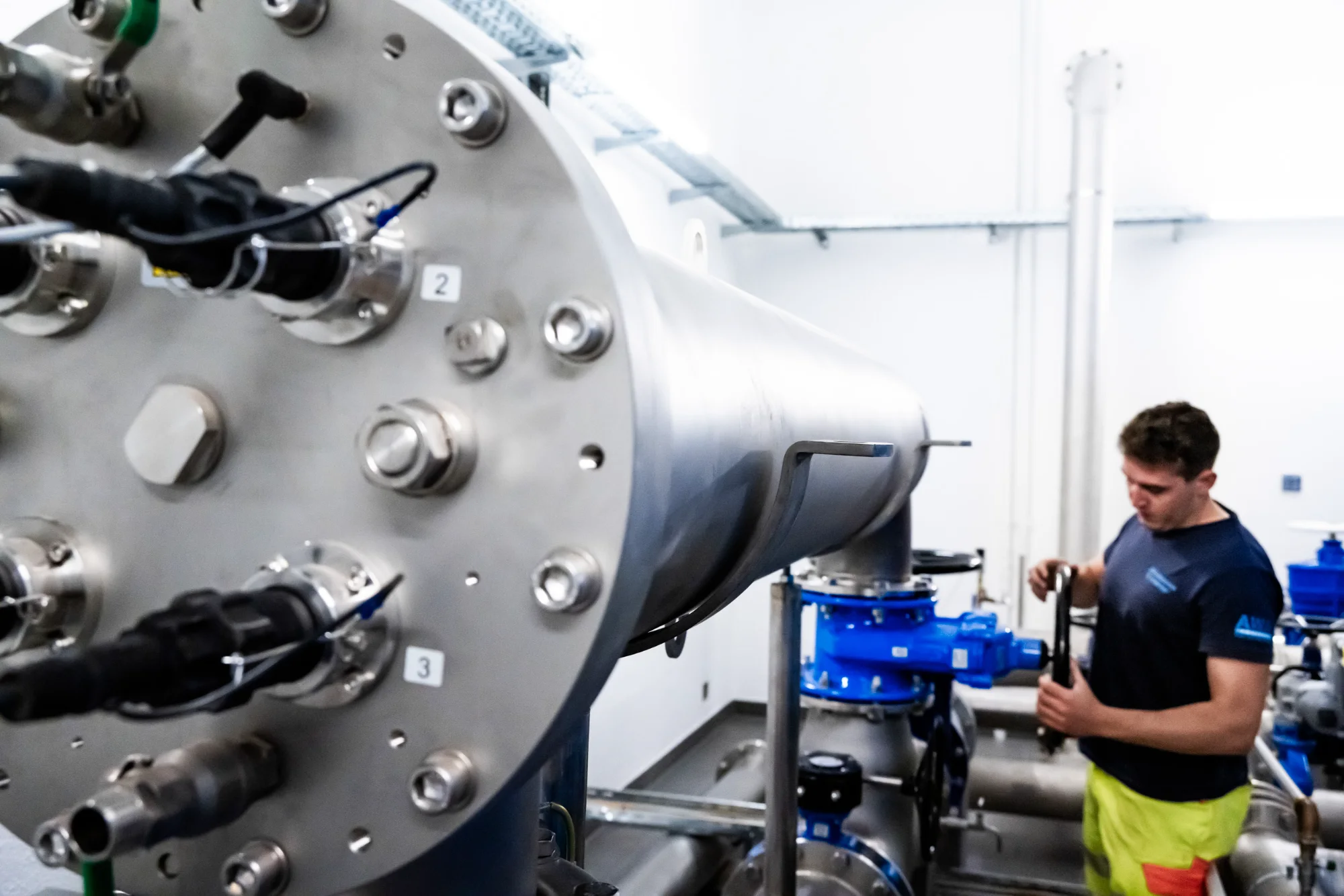 Technician in hi-vis trousers at a large stainless steel filter vessel in the waterworks — AWA Ammersee, industrial, corporate and portrait photography by Janina Laszlo