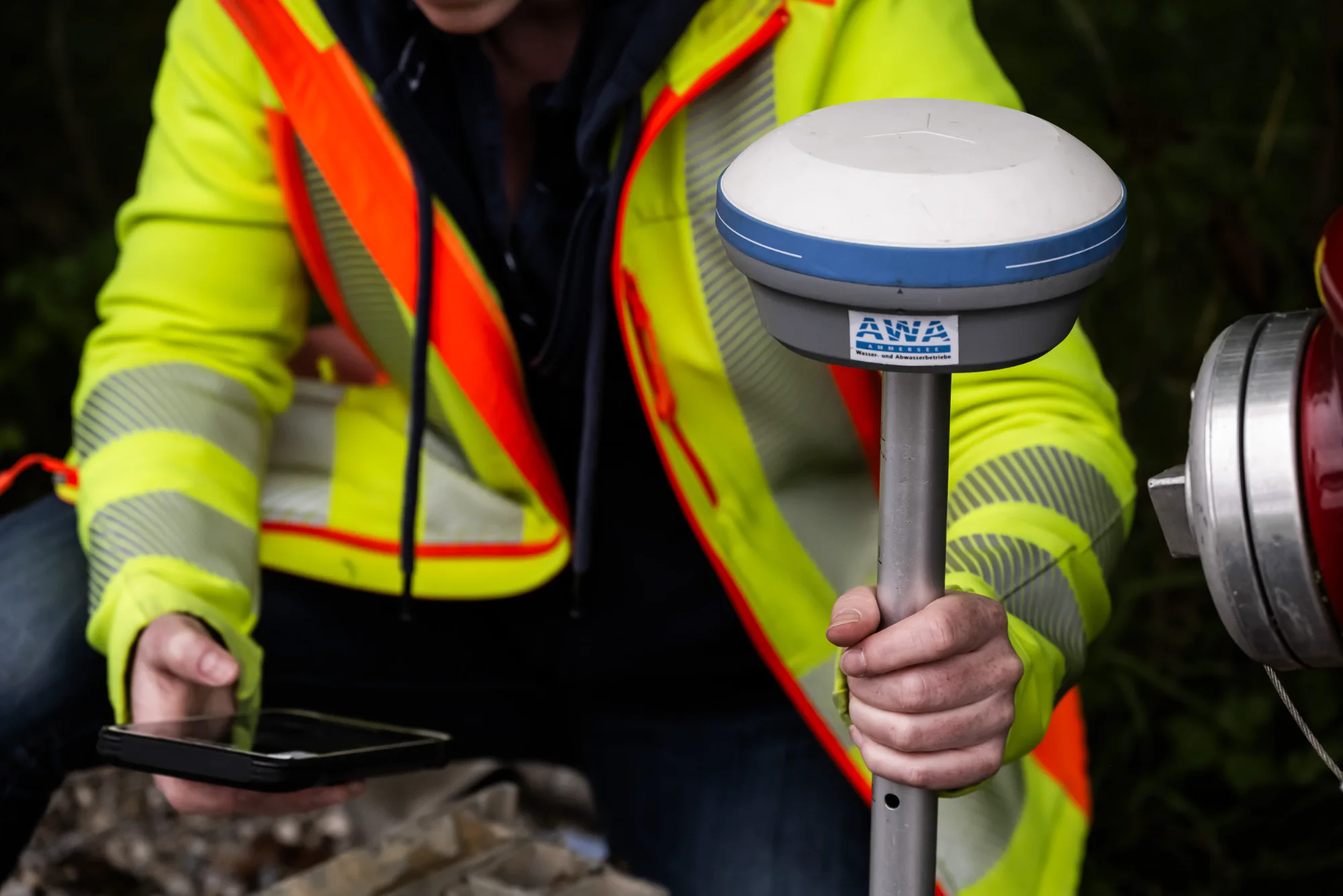 Hands in a hi-vis jacket operating a GNSS receiver with AWA logo, close-up — AWA Ammersee, industrial, corporate and portrait photography by Janina Laszlo
