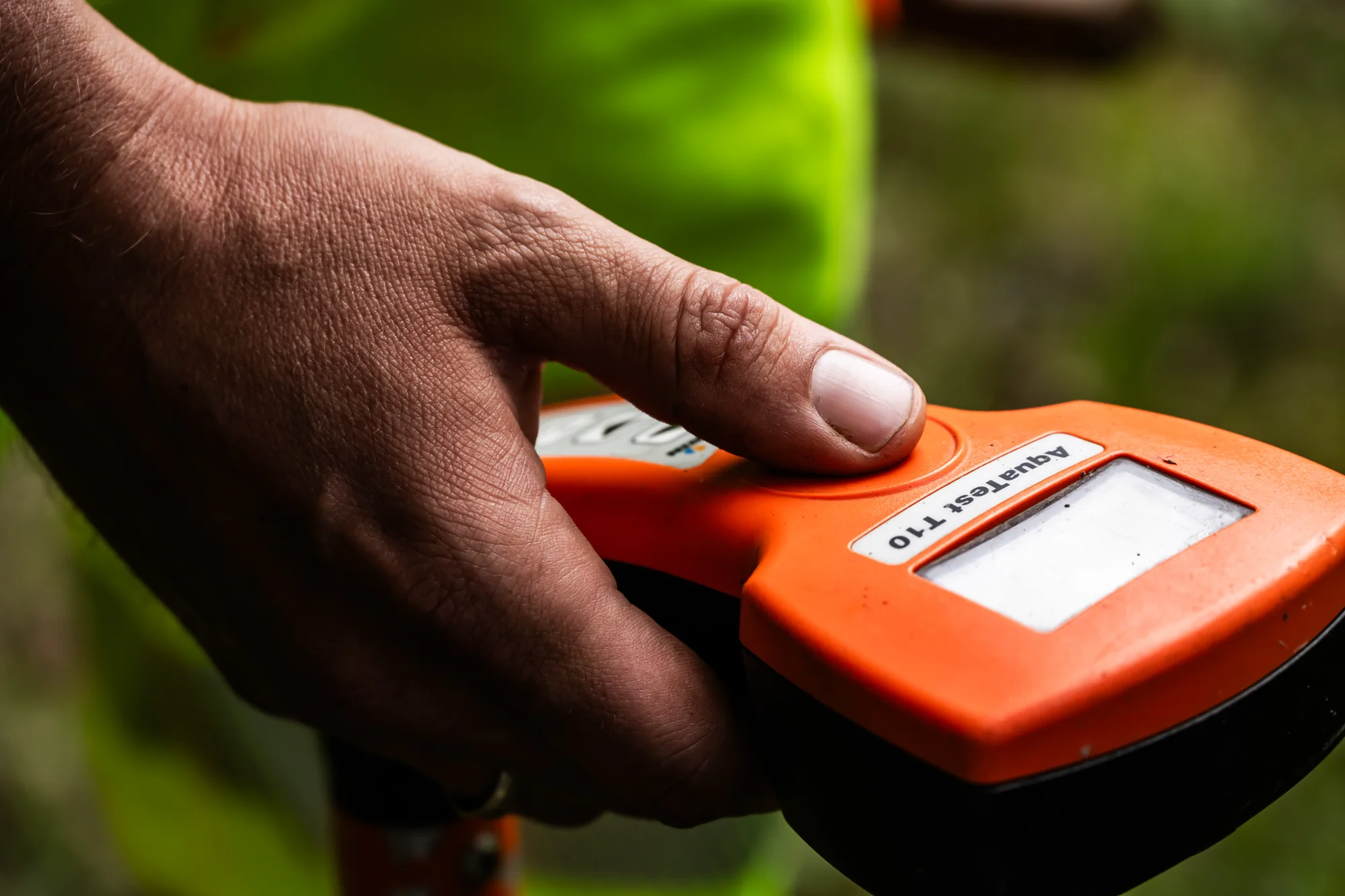 Hand pressing the button of an orange leak-detection device, close-up — AWA Ammersee, industrial, corporate and portrait photography by Janina Laszlo