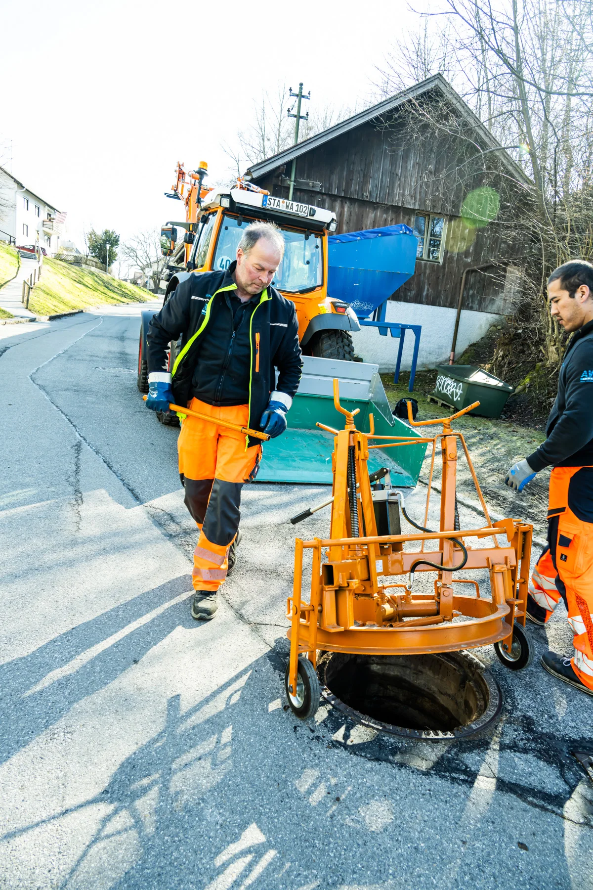 Crew in orange workwear with a manhole winch on a village street — AWA Ammersee, industrial, corporate and portrait photography by Janina Laszlo