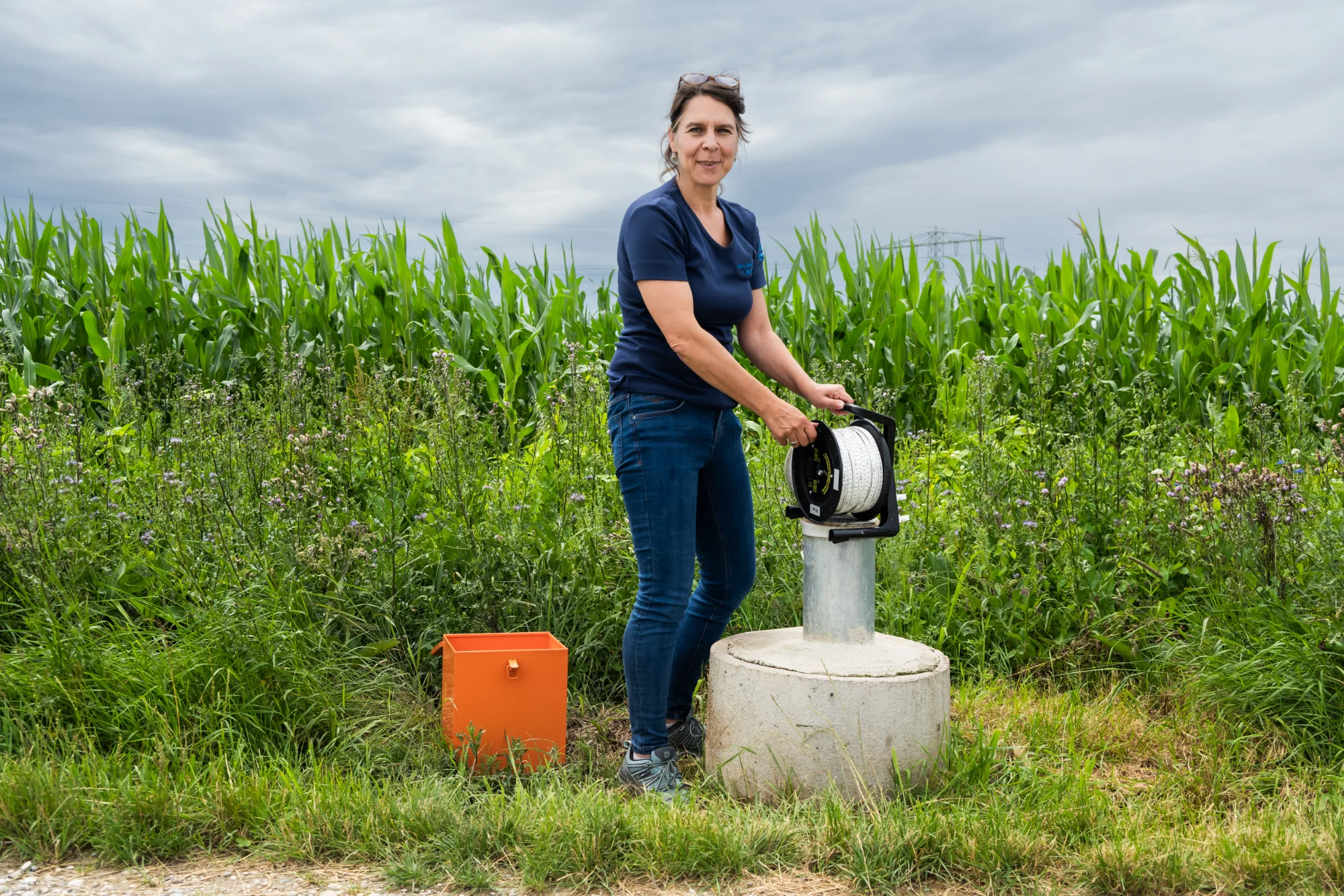 Woman measuring groundwater at a monitoring well beside a maize field — AWA Ammersee, industrial, corporate and portrait photography by Janina Laszlo