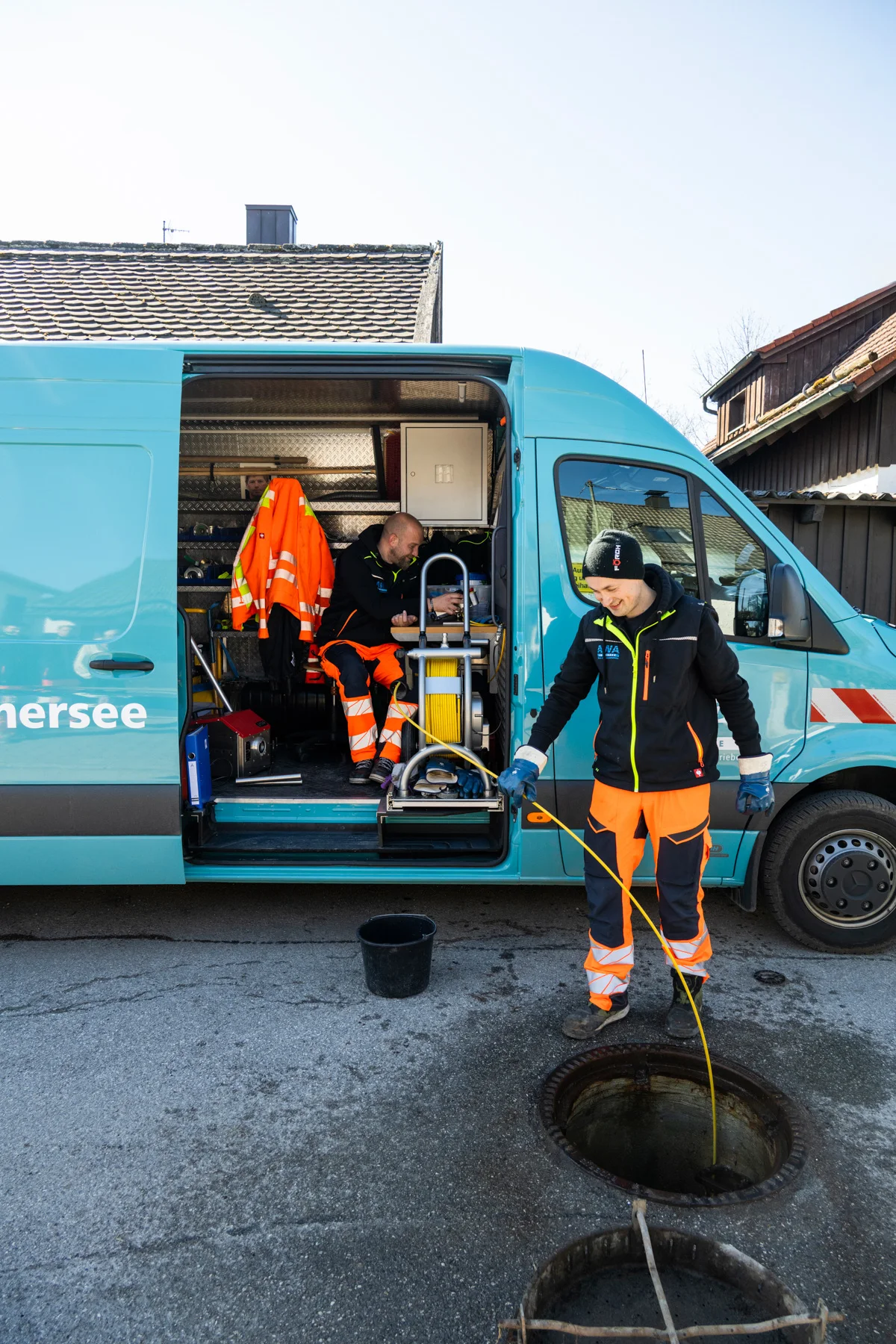 Sewer worker at an open manhole beside the turquoise AWA service van — AWA Ammersee, industrial, corporate and portrait photography by Janina Laszlo