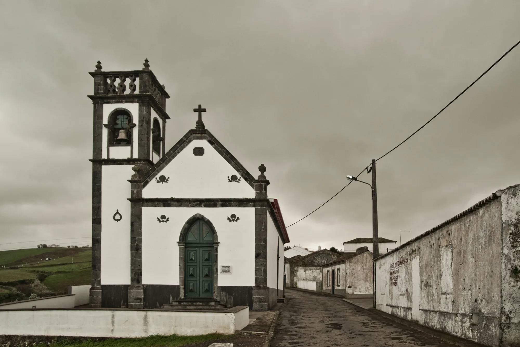 White chapel with dark basalt trim on an empty village street under grey sky — Azores, São Miguel, travel and fine art photography by Janina Laszlo