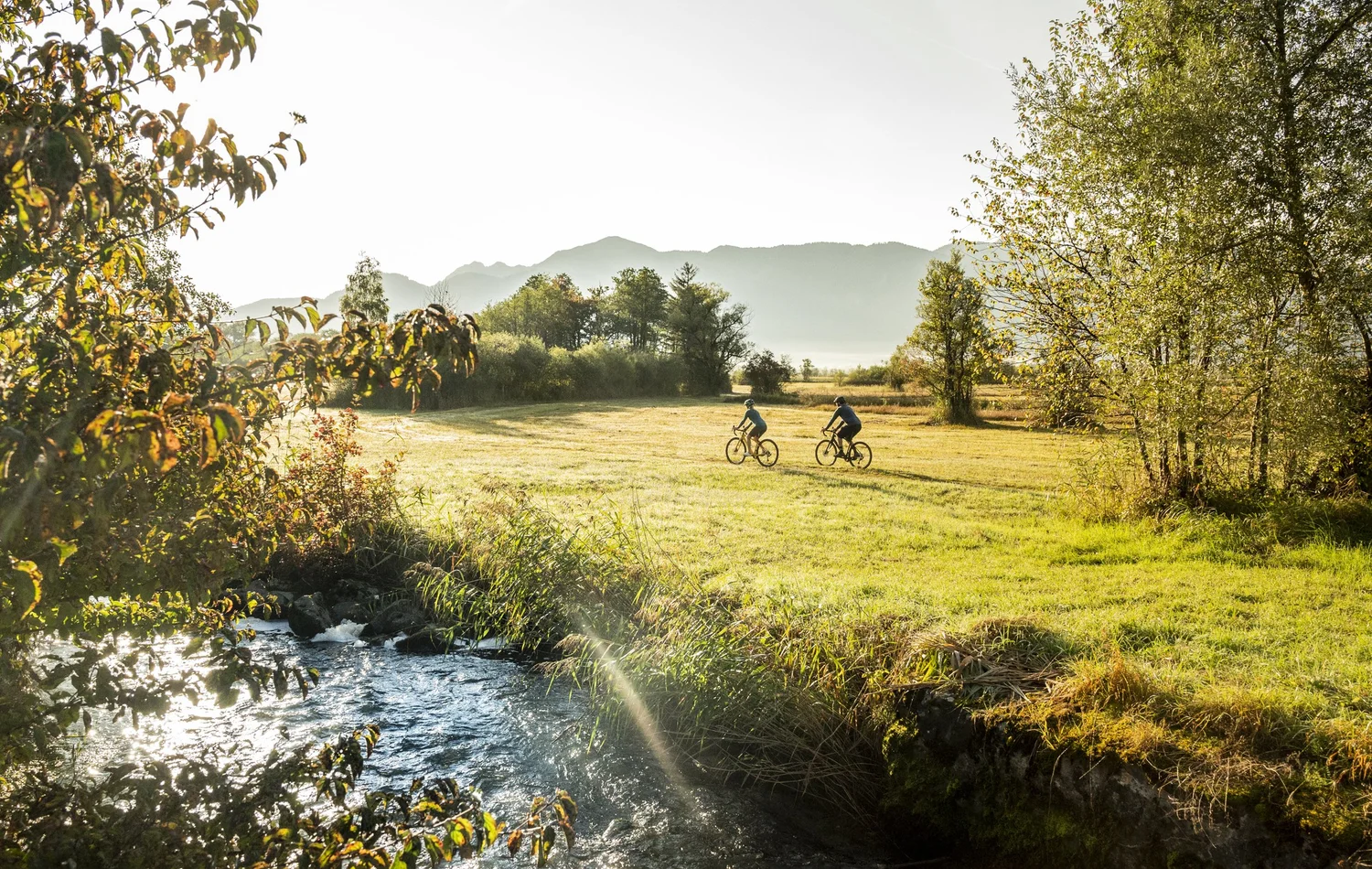 Cyclists riding along a sunlit brook in autumn colours, Blaues Land tourism campaign — campaign photography by Janina Laszlo, Munich