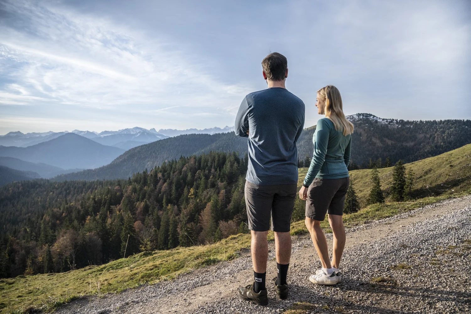 Hiking couple looking out over the Bavarian Alps from a gravel mountain trail — campaign photography by Janina Laszlo, Munich