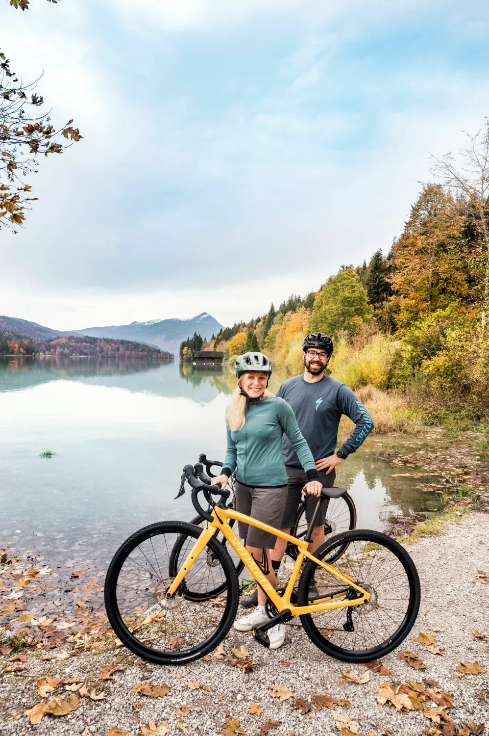 Couple with e-bikes on the shore of an Alpine lake in autumn, Blaues Land, Bayerischer Tourismusverband — campaign photography by Janina Laszlo, Munich