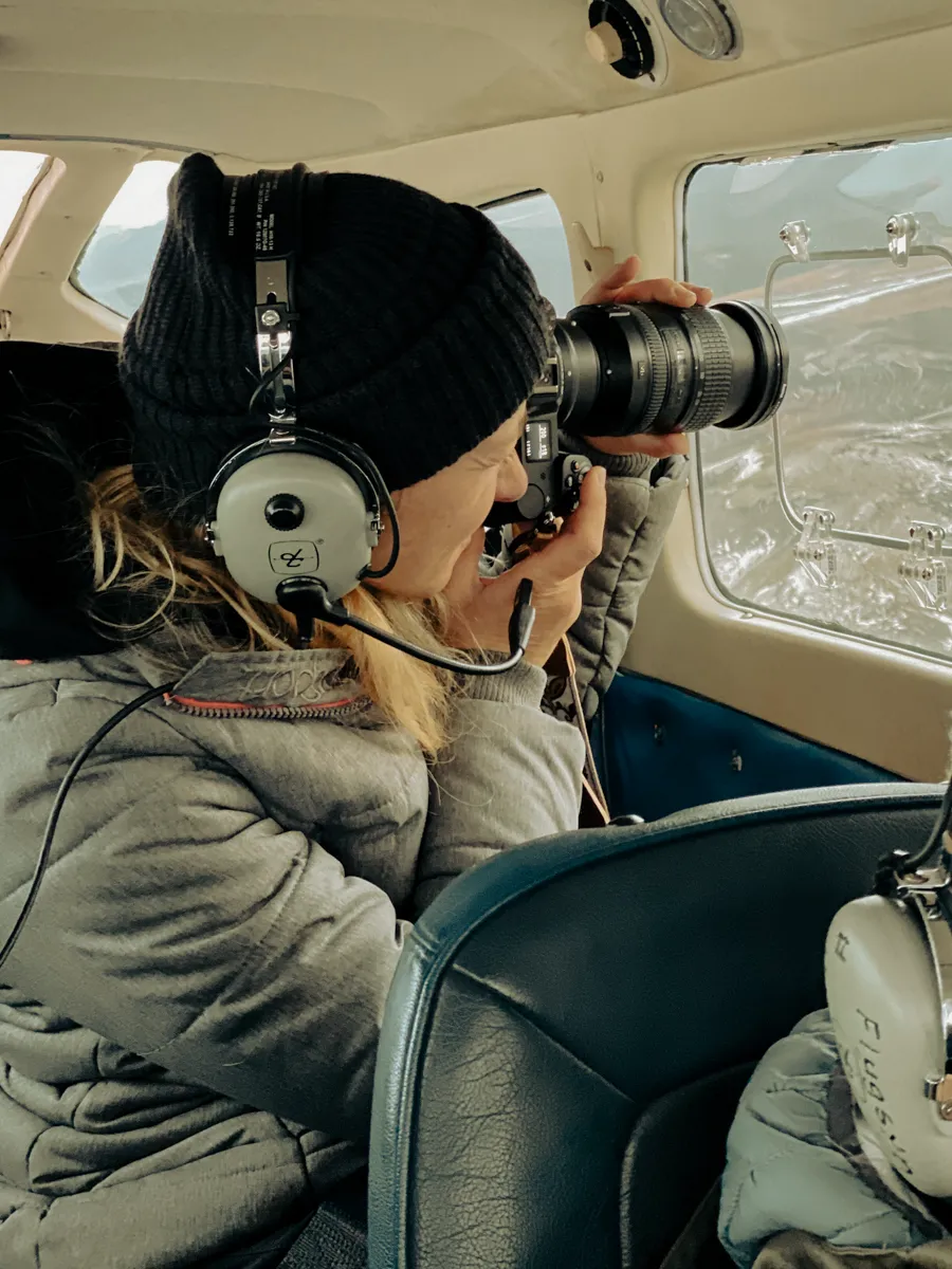 Behind the scenes with Janina Laszlo, German commercial and editorial photographer, shooting through the window of a small aircraft over Iceland with headset and telephoto lens during a professional photography production