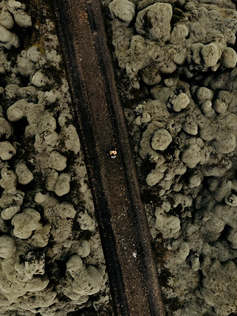 Drone view of Janina Laszlo on a dark gravel road through a moss-covered lava field in Iceland — behind the scenes with the German commercial and editorial photographer
