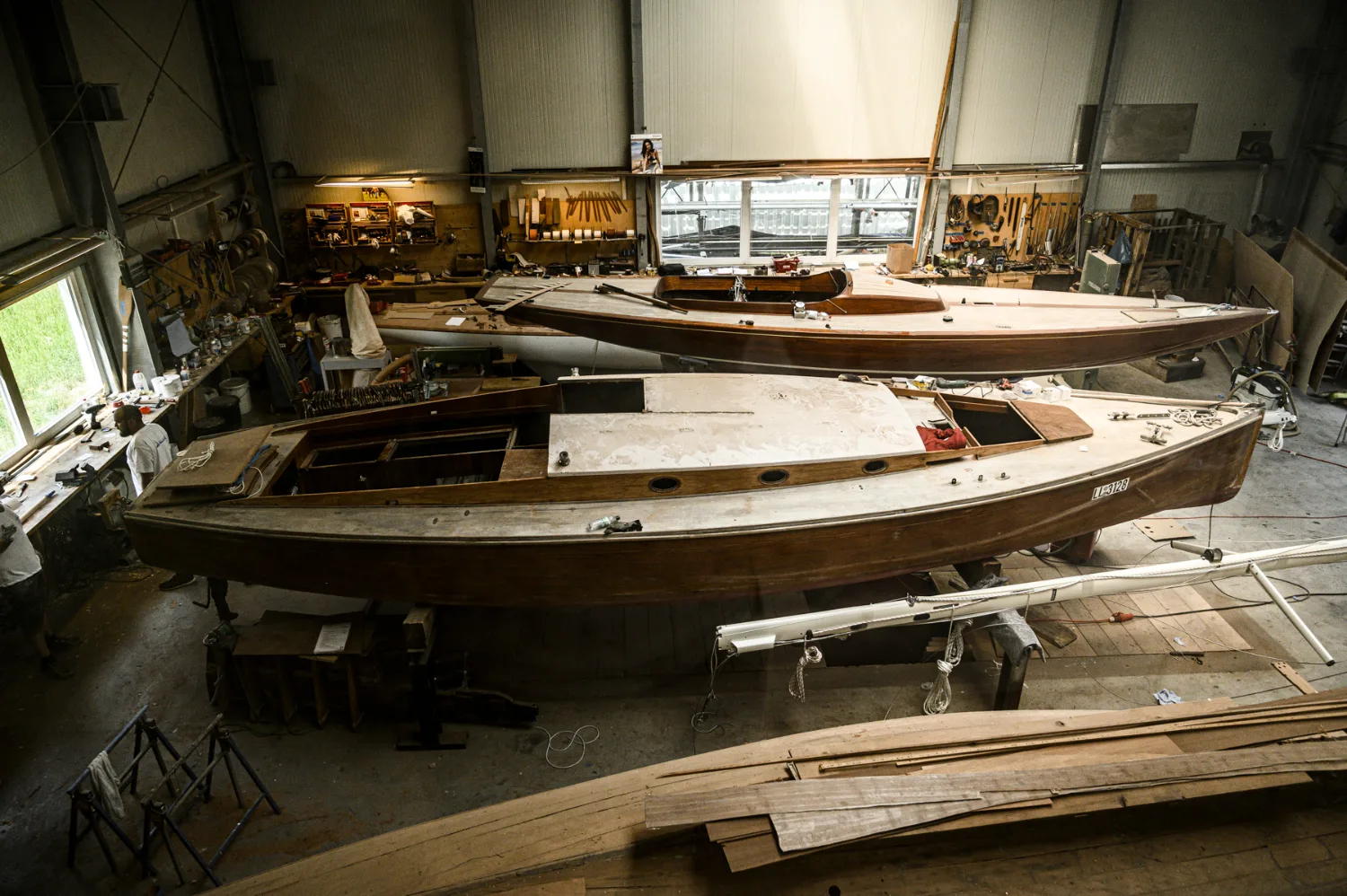 Two classic wooden sailing boats under restoration in the Bootsbau Liebner workshop hall at the Ammersee — commercial and editorial photography by Janina Laszlo, photographer in Munich