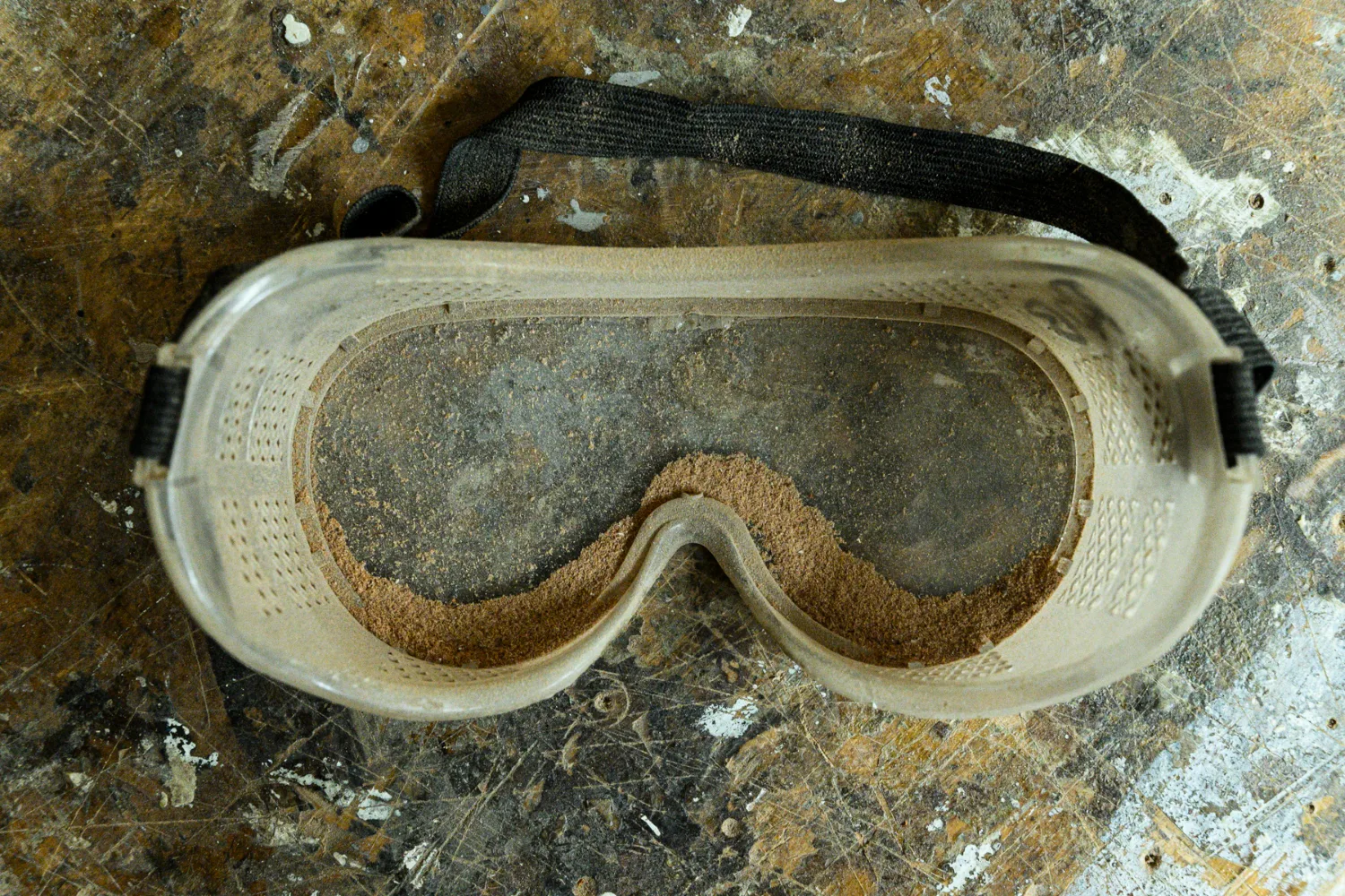 Safety goggles filled with fine wood dust on a scarred workbench — commercial and editorial photography by Janina Laszlo, photographer in Munich