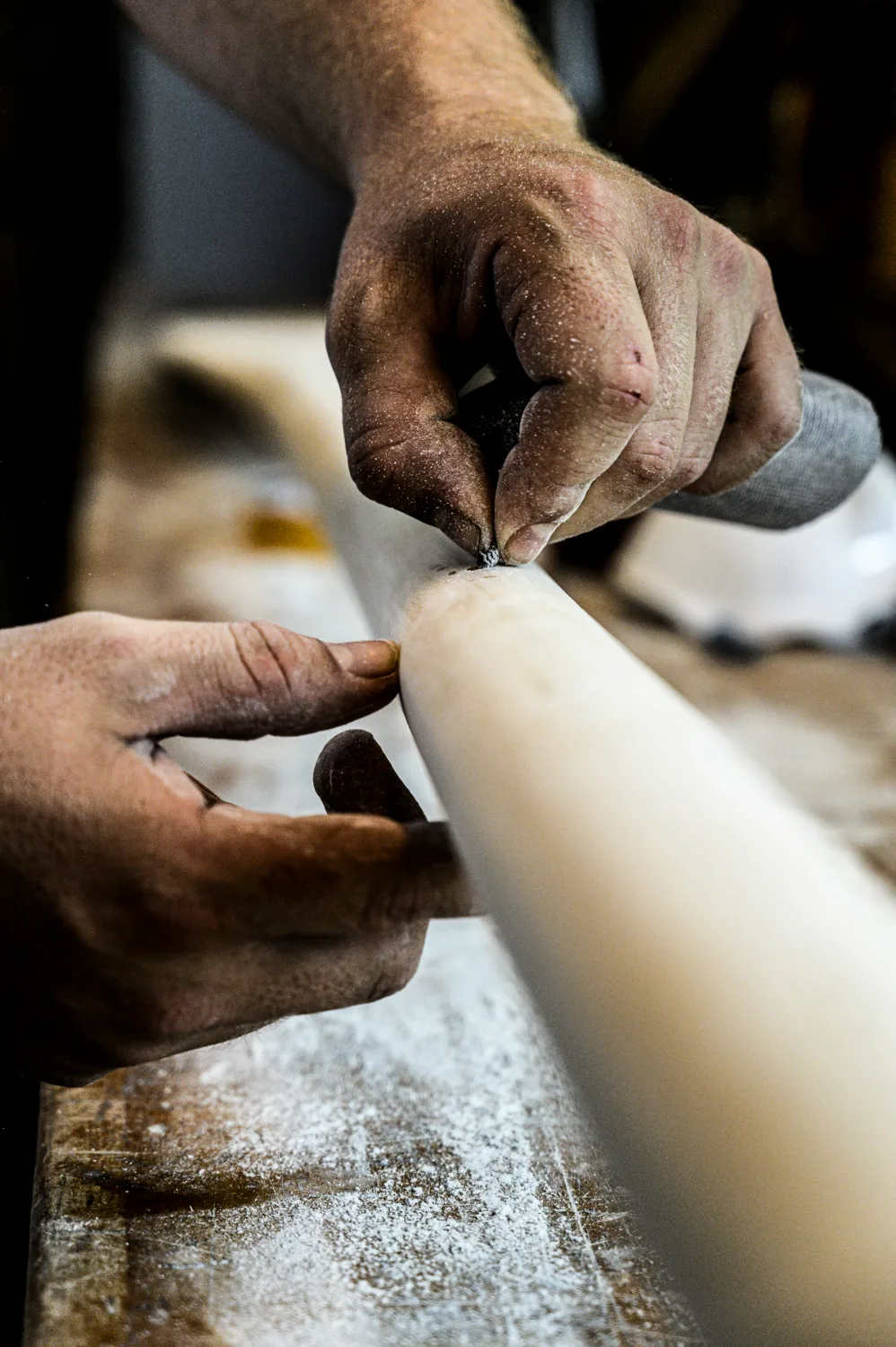 Hands sanding and filling a white wooden mast on a dusty workbench — commercial and editorial photography by Janina Laszlo, photographer in Munich
