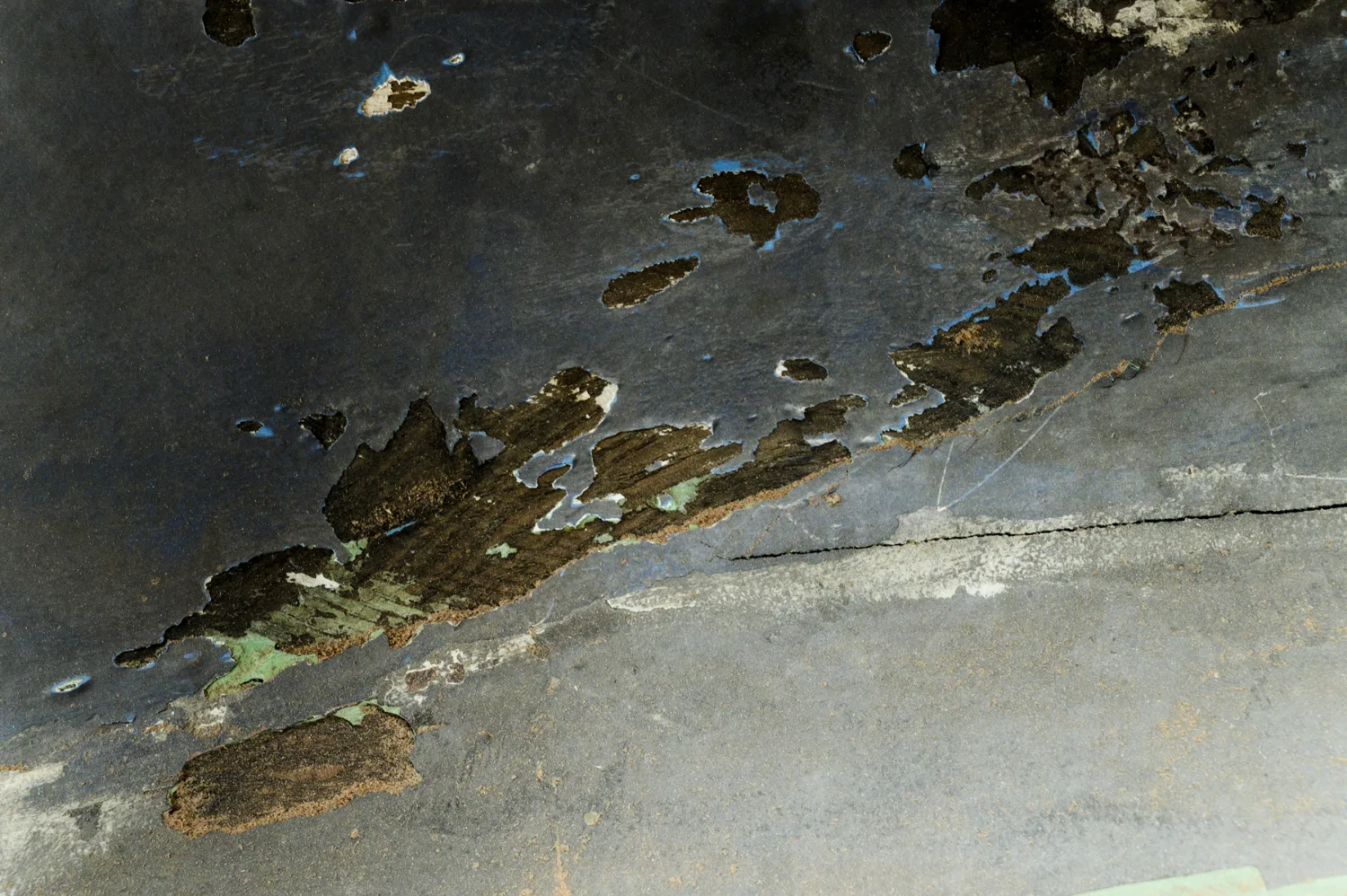 Peeling dark antifouling paint exposing old timber on an upturned hull — commercial and editorial photography by Janina Laszlo, photographer in Munich