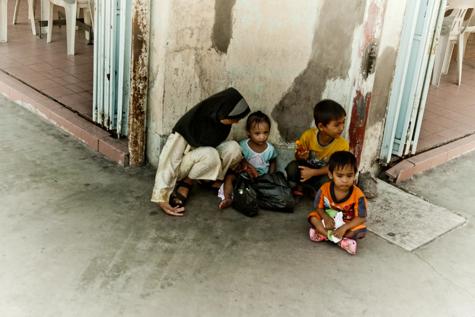 Mother and three children resting against a weathered pillar on a pavement — Borneo & Pulau Mabul, documentary and travel photography by Janina Laszlo