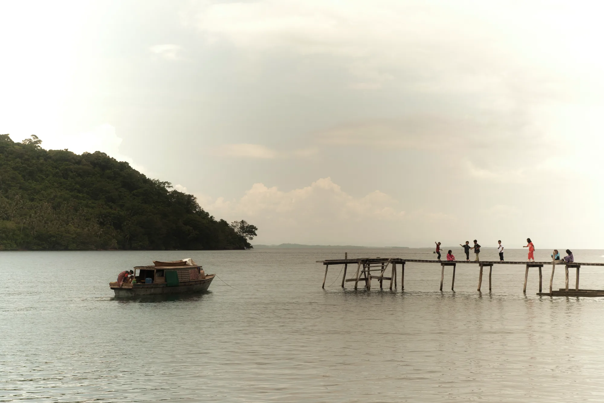 Wooden boat and children on a long jetty beside a forested island — Borneo & Pulau Mabul, documentary and travel photography by Janina Laszlo