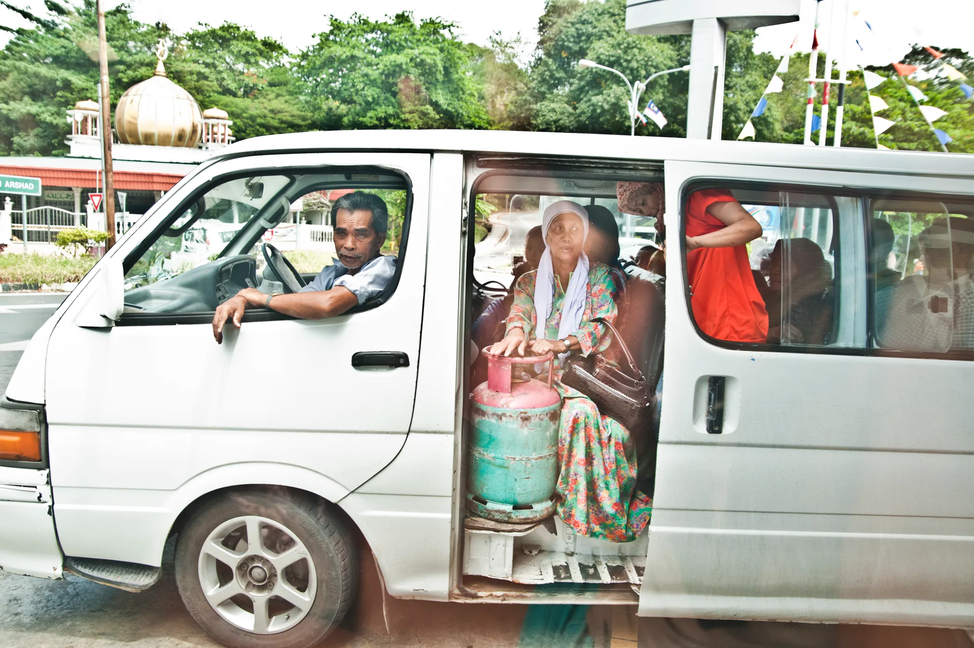 Minibus driver and passengers, a woman holding a gas cylinder in the open door — Borneo & Pulau Mabul, documentary and travel photography by Janina Laszlo
