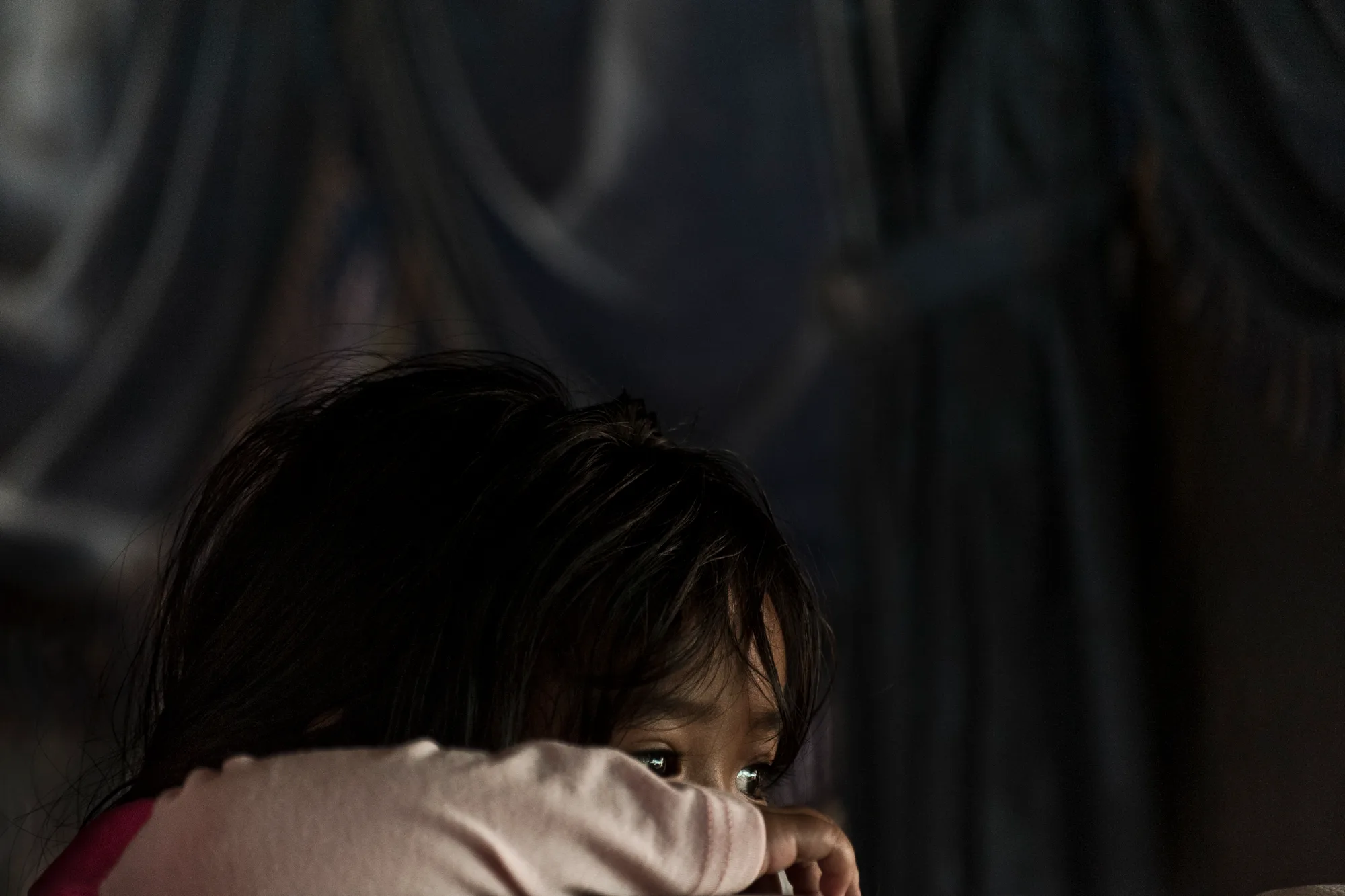 Girl peeking over her arm in dim light — Borneo & Pulau Mabul, documentary and travel photography by Janina Laszlo