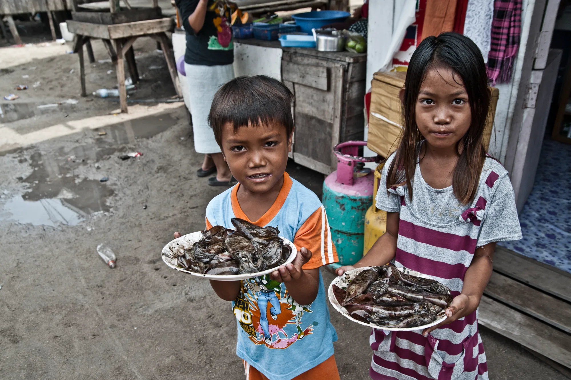 Boy and girl holding plates of fresh squid — Borneo & Pulau Mabul, documentary and travel photography by Janina Laszlo