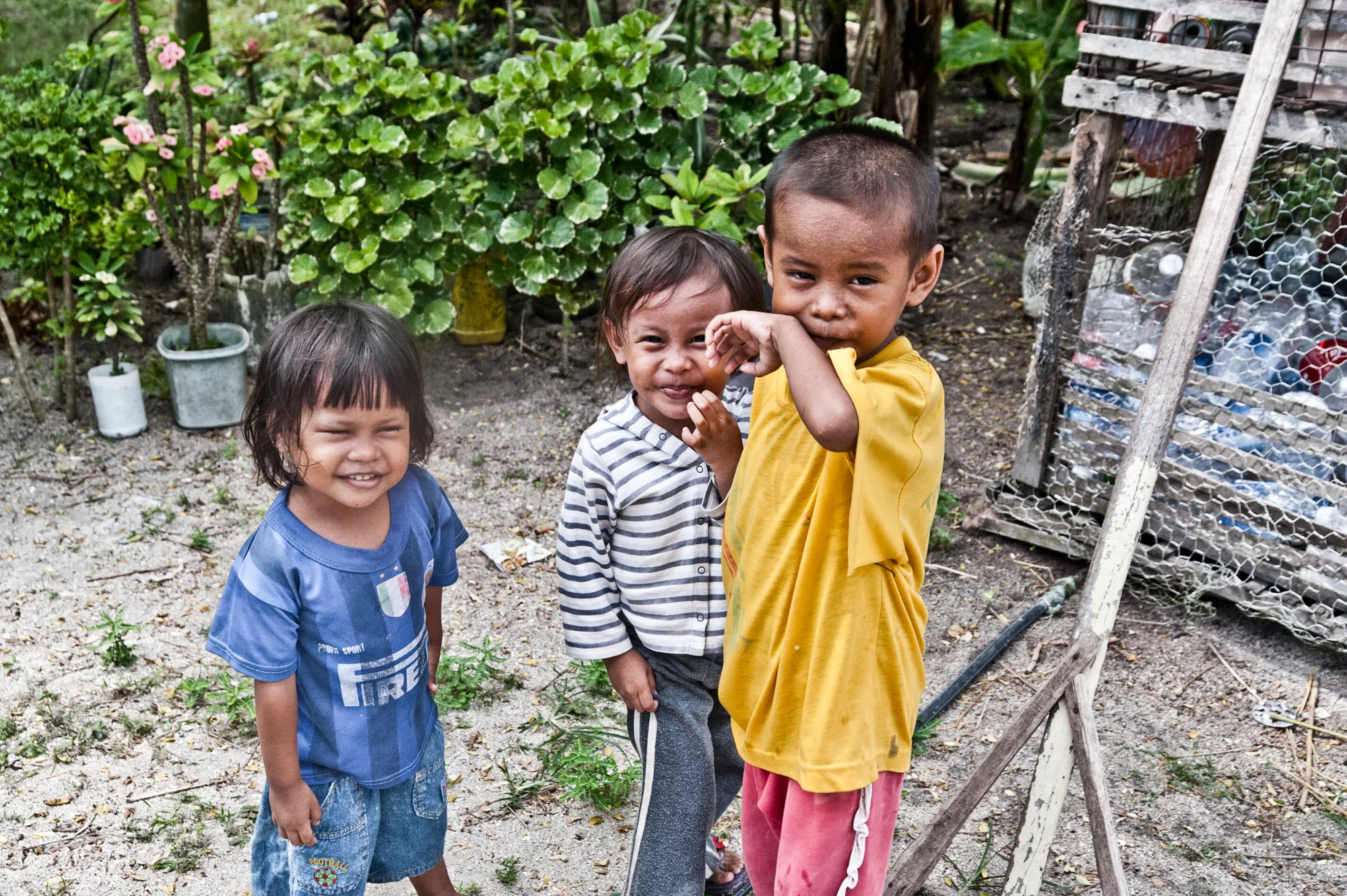Three smiling children in front of a garden — Borneo & Pulau Mabul, documentary and travel photography by Janina Laszlo