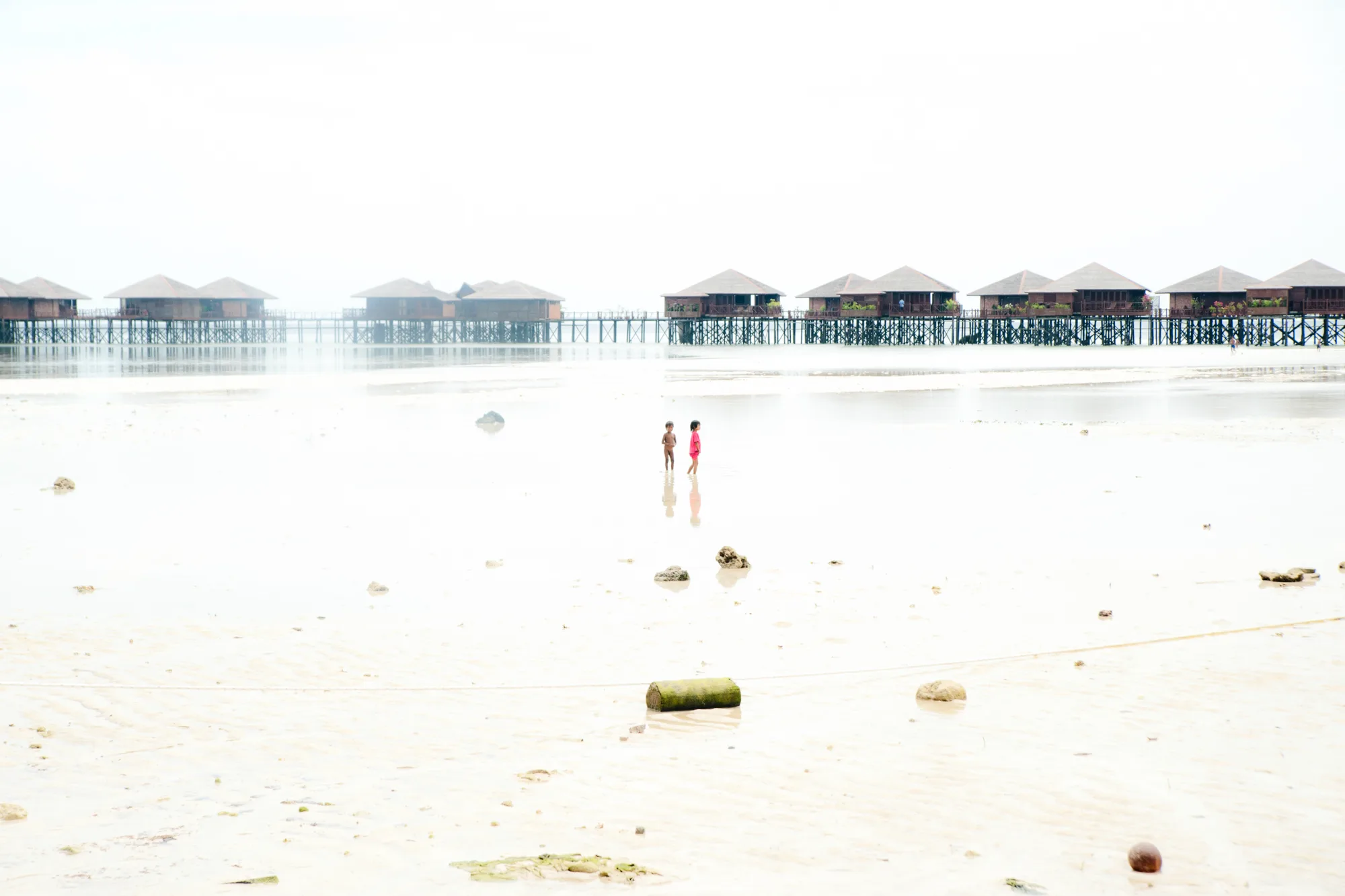 Two children on the tidal flats before overwater villas, Pulau Mabul, Sabah — Borneo & Pulau Mabul, documentary and travel photography by Janina Laszlo