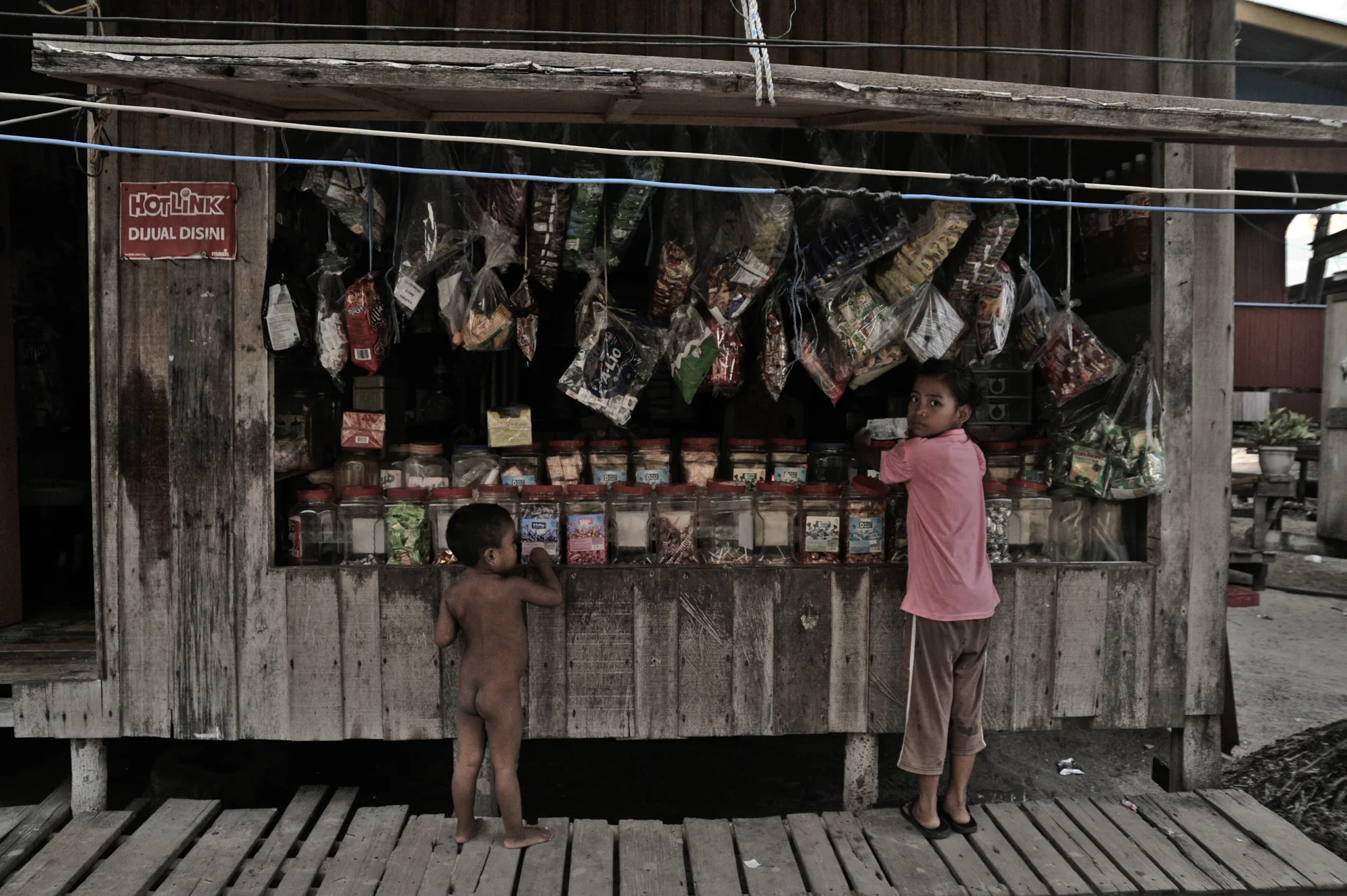 Two children at a wooden sweet kiosk with jars of candy — Borneo & Pulau Mabul, documentary and travel photography by Janina Laszlo