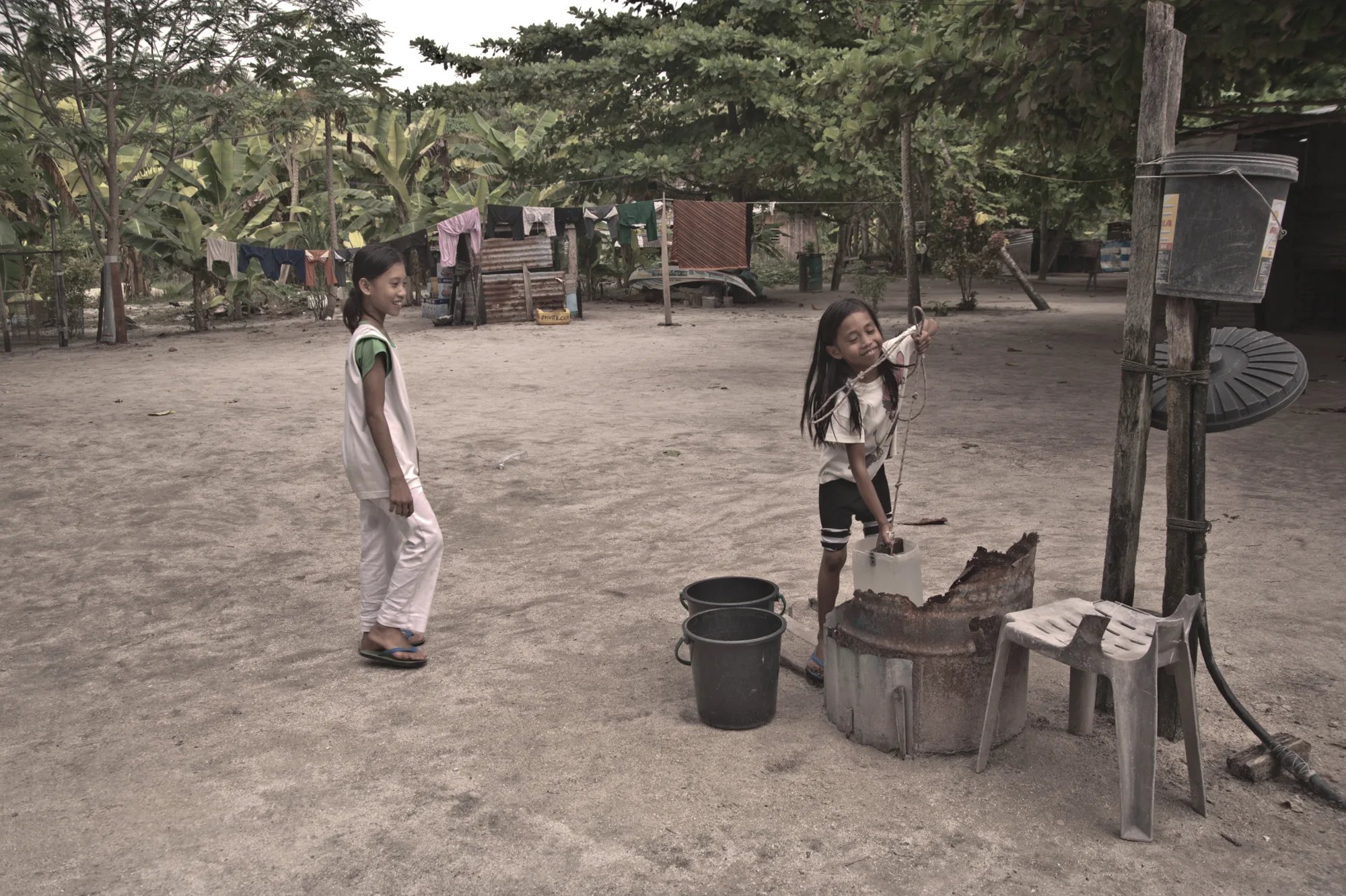 Two girls drawing water from a well with buckets — Borneo & Pulau Mabul, documentary and travel photography by Janina Laszlo