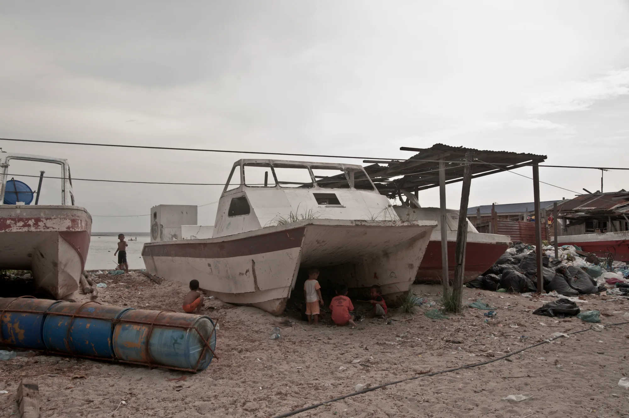 Children playing in the shade under a beached catamaran — Borneo & Pulau Mabul, documentary and travel photography by Janina Laszlo