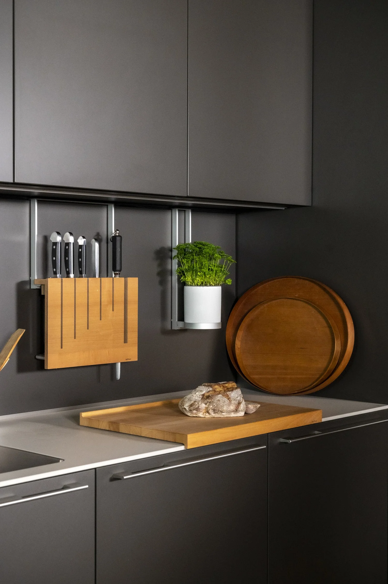 Dark bulthaup kitchen wall with knife rail, round cutting board and fresh herbs — campaign photography by Janina Laszlo, Munich