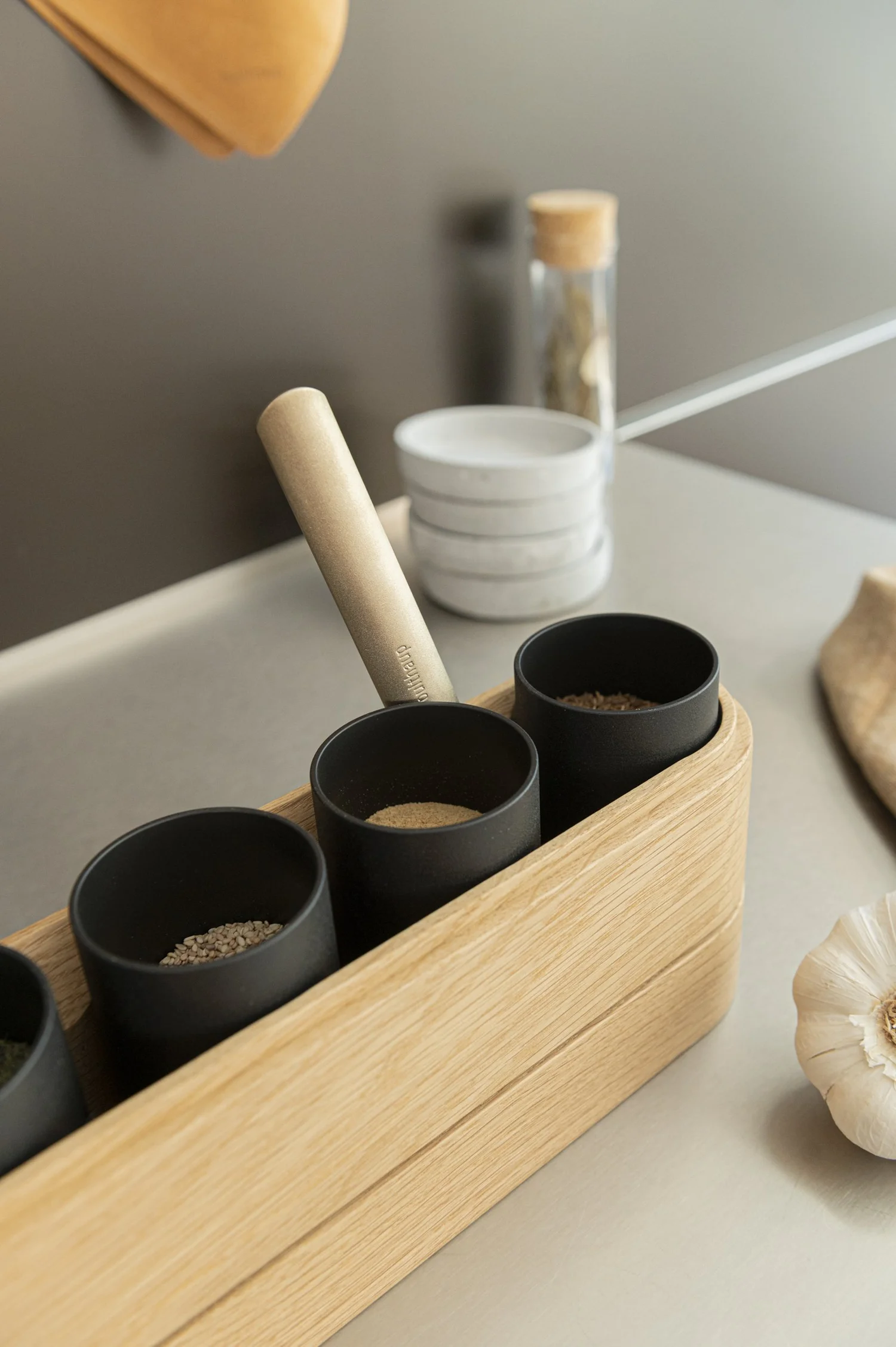 Black spice tubs in an oak holder with a wooden pestle on a bulthaup worktop — campaign photography by Janina Laszlo, Munich
