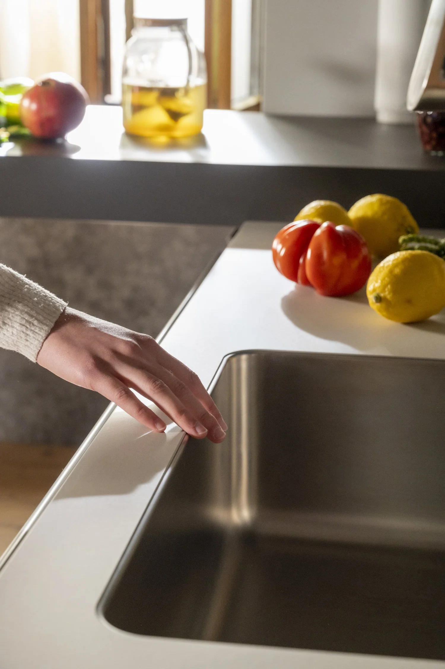 Hand wiping a stainless steel bulthaup sink next to tomatoes and lemons — campaign photography by Janina Laszlo, Munich