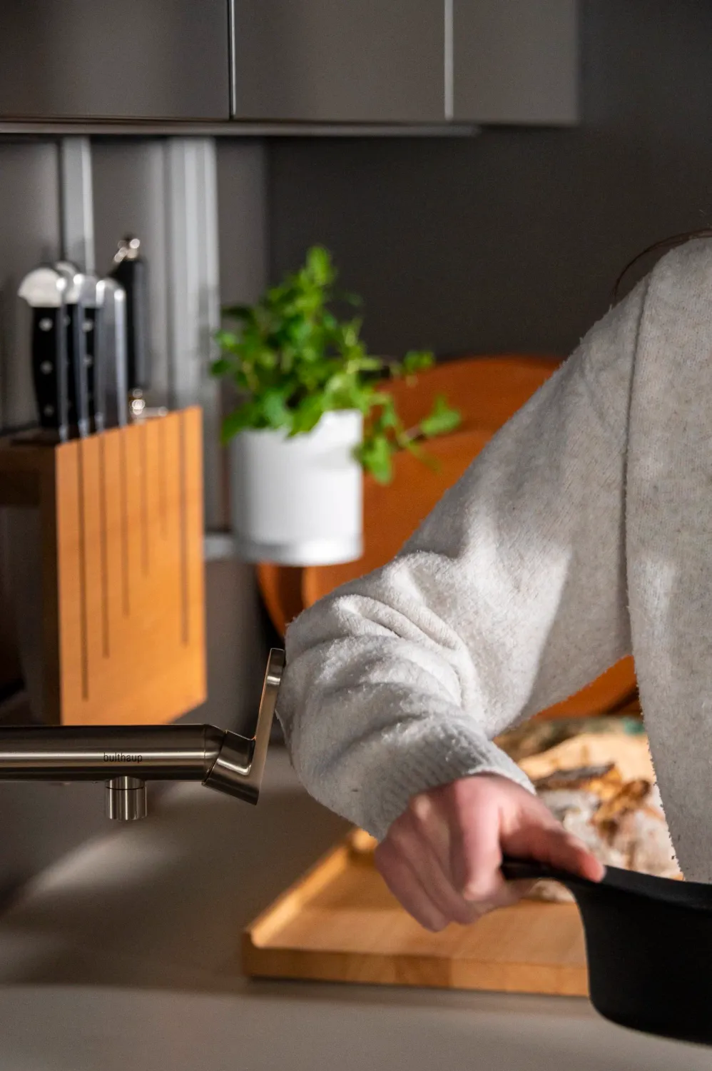Cook slicing pizza next to a knife block and basil in a bulthaup kitchen — campaign photography by Janina Laszlo, Munich