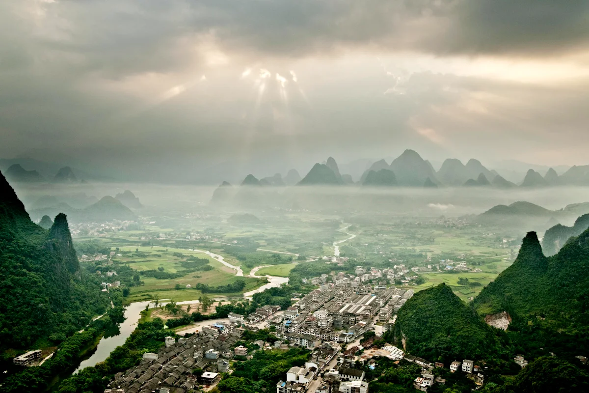Sunbeams breaking through clouds over karst peaks and a river valley near Xingping, Guangxi — China, documentary and travel photography by Janina Laszlo