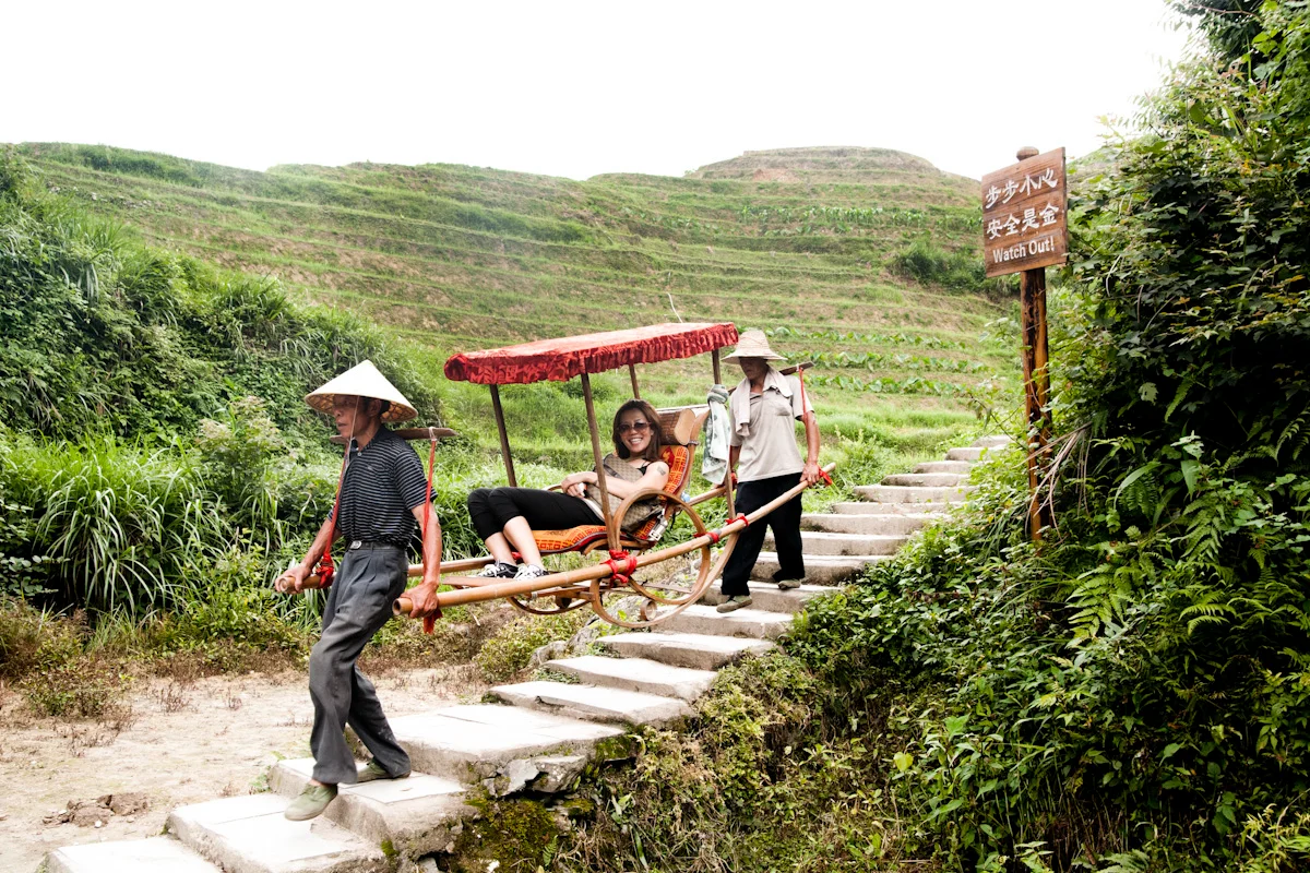 Porters carrying a tourist in a sedan chair up stone steps through rice terraces, Guangxi — China, documentary and travel photography by Janina Laszlo