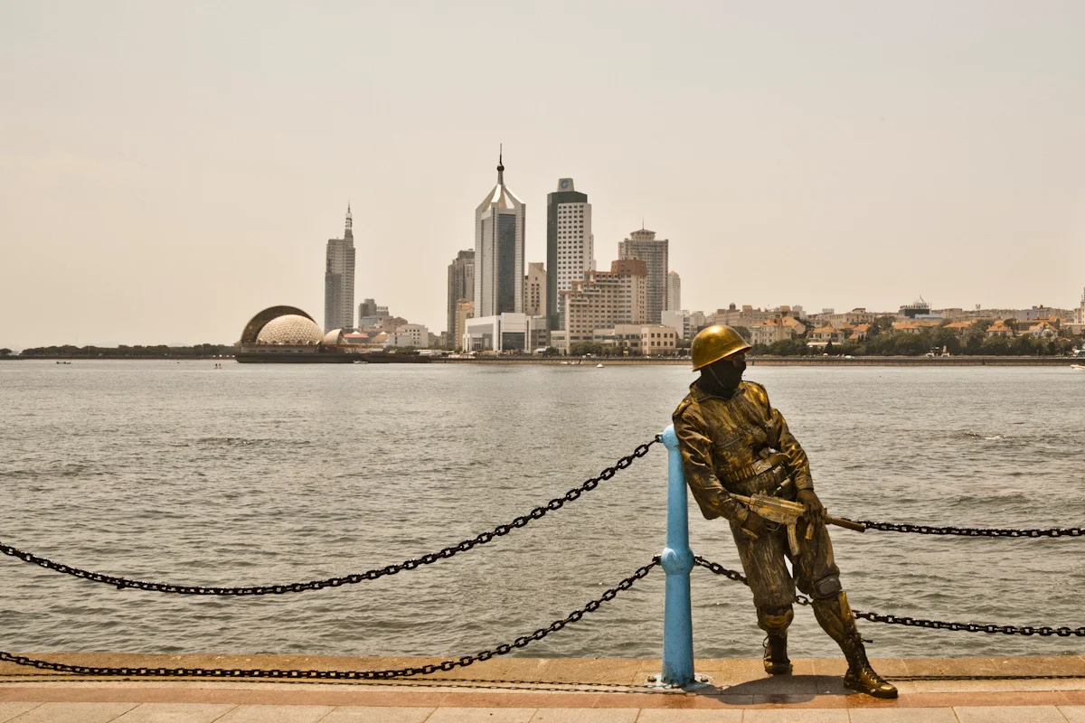 Bronze soldier statue at a waterfront railing before the skyline, Qingdao — China, documentary and travel photography by Janina Laszlo